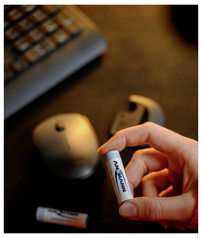 Une main tenant une petite pile AAA au-dessus d'un bureau avec une souris et un clavier en arrière-plan.