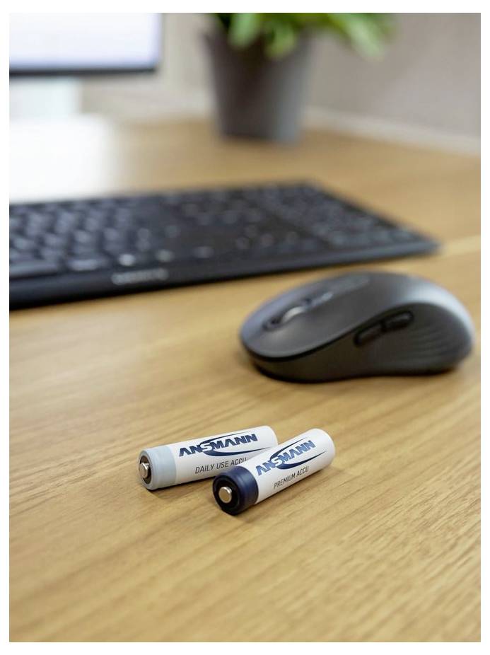 Deux batteries Ansmann AA sur un bureau en bois à côté d'une souris sans fil noire et d'un clavier.