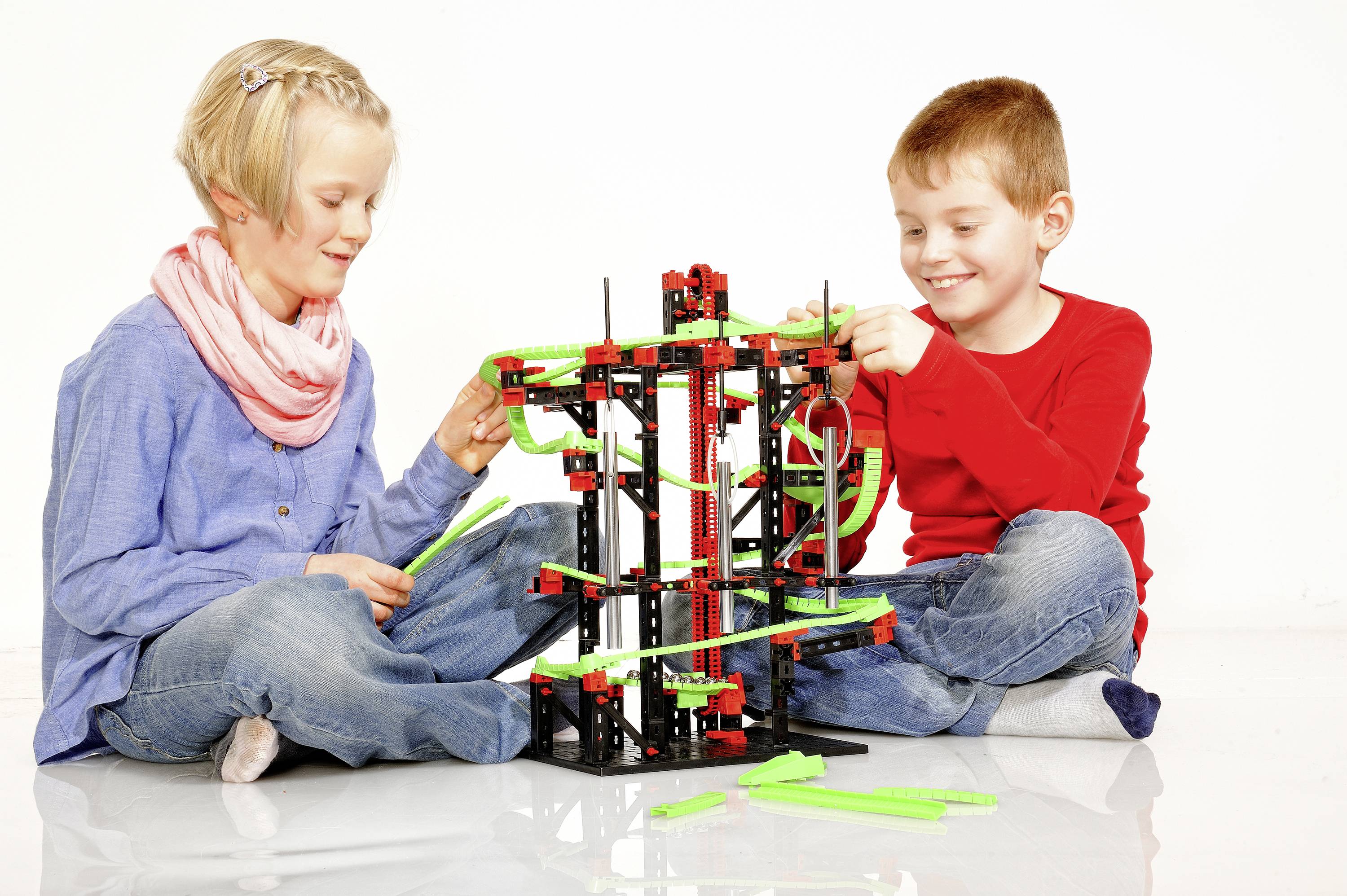 Deux enfants construisent ensemble un modèle de jeu de construction avec des pièces colorées. Ils sont assis par terre et sourient.