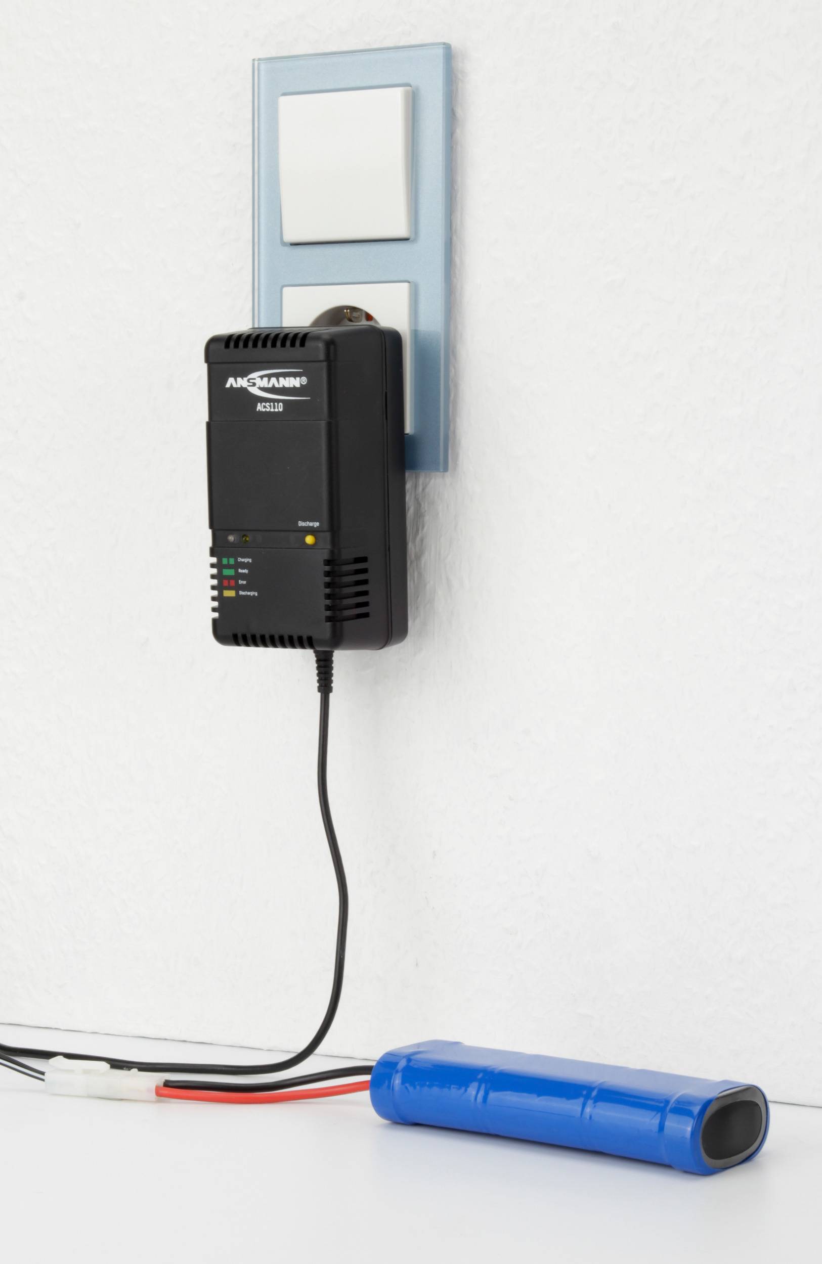 Un chargeur est branché à une prise électrique et charge une batterie bleue sur une table. Il affiche des voyants indiquant l'état de charge.