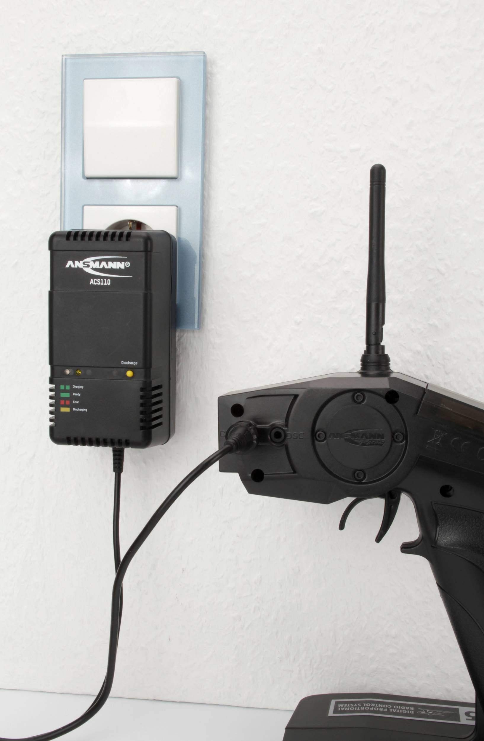 Le télécommande est en charge à une prise murale avec un chargeur Ansmann. Les voyants LED indiquent l'état de la charge.