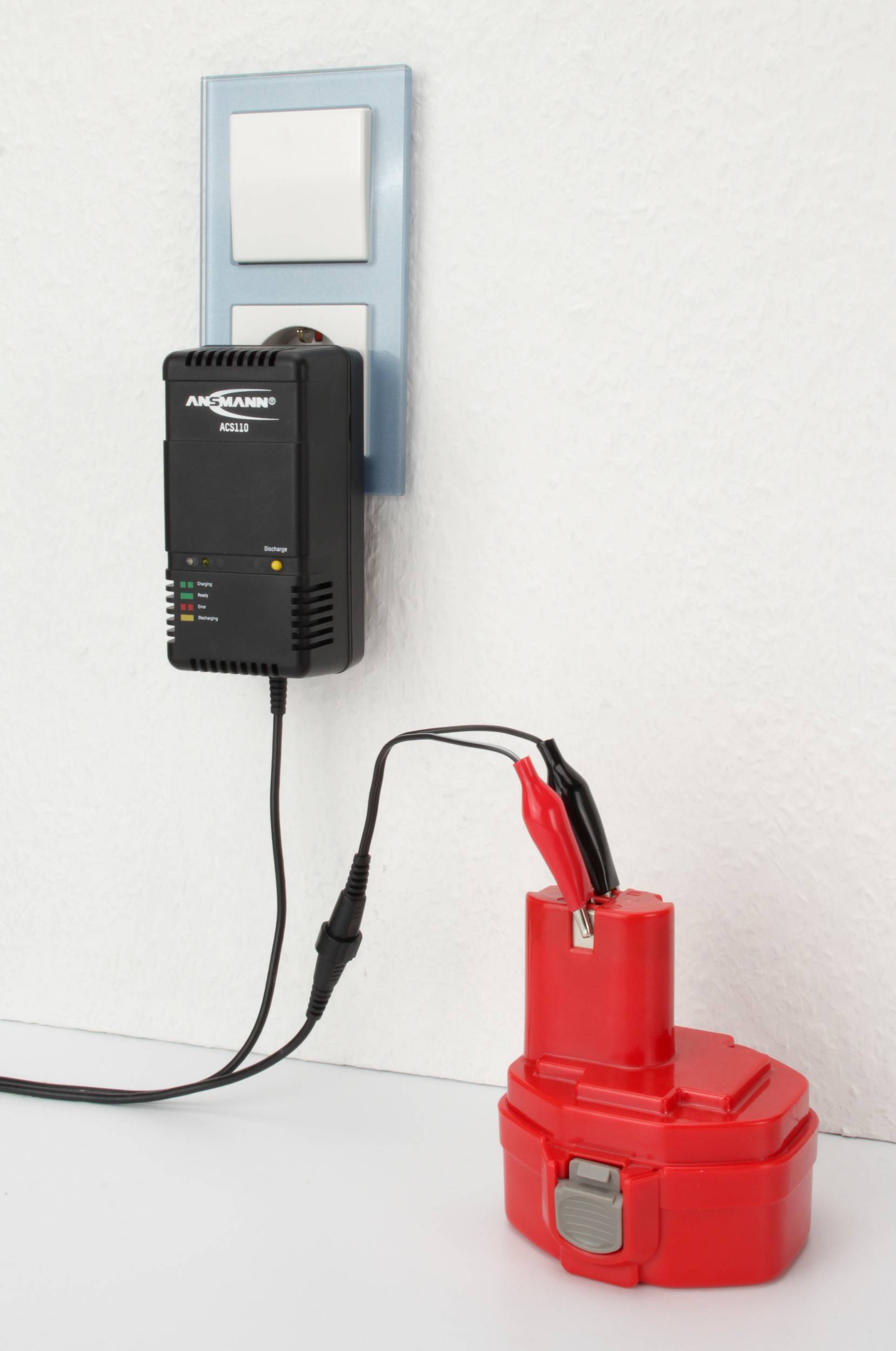 Une batterie rouge est branchée à une prise électrique via un chargeur. Le chargeur indique l'état de charge à l'aide de diodes électroluminescentes.