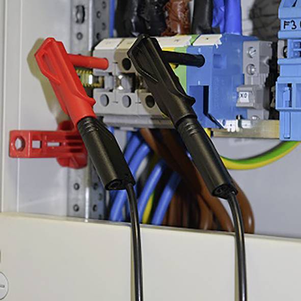 Un intérieur de tableau électrique avec des pointes de test rouges et noires connectées à un câble.