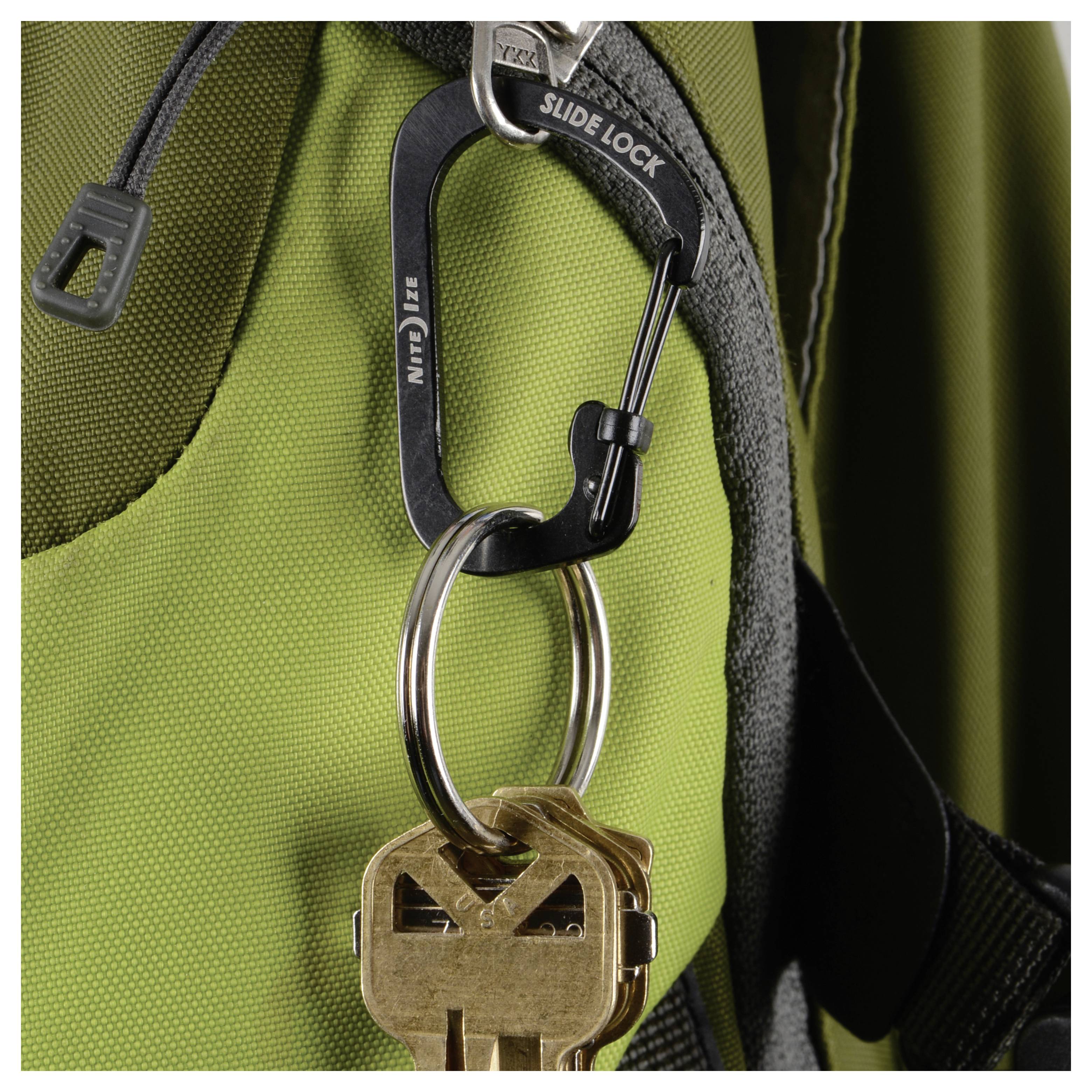 Un mousqueton portant l'étiquette « Slide Lock » retient deux clés sur la sangle d'un sac à dos.