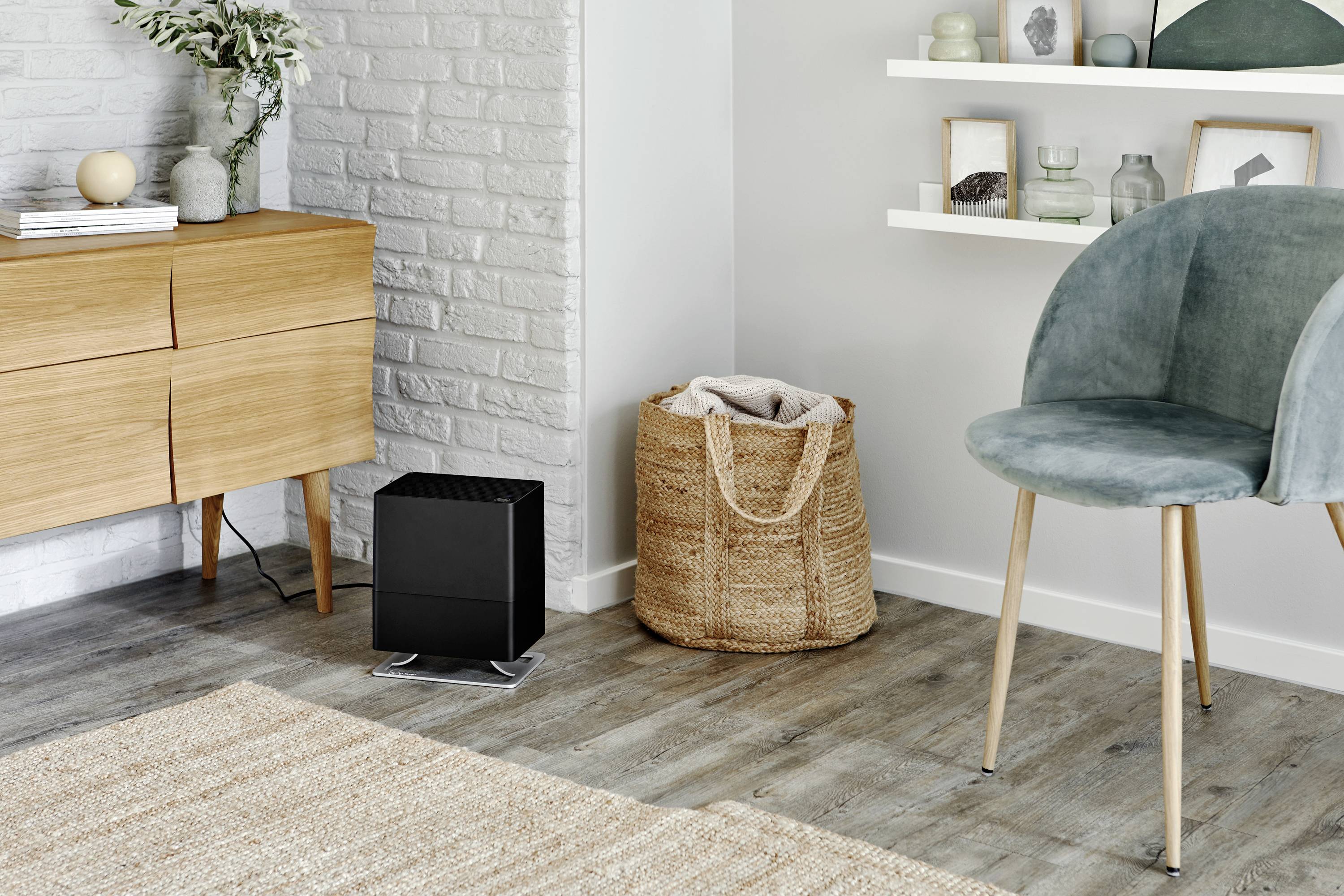 Un salon élégant avec des meubles en bois, un fauteuil et des éléments de décoration. Un purificateur d'air noir est posé sur le sol.