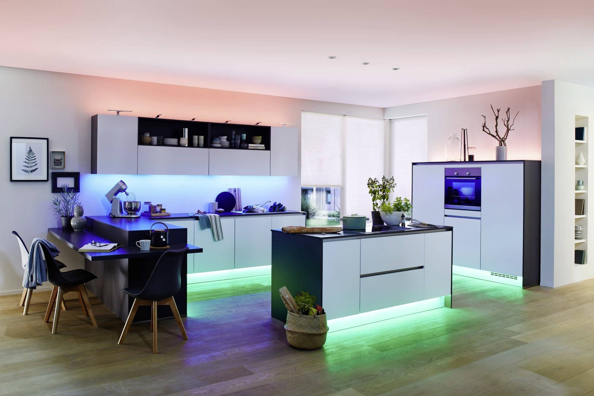 Cuisine moderne avec des armoires éclairées en bleu et vert. Îlot central avec un plan de travail noir. Sols en bois clair, agencement ouvert.