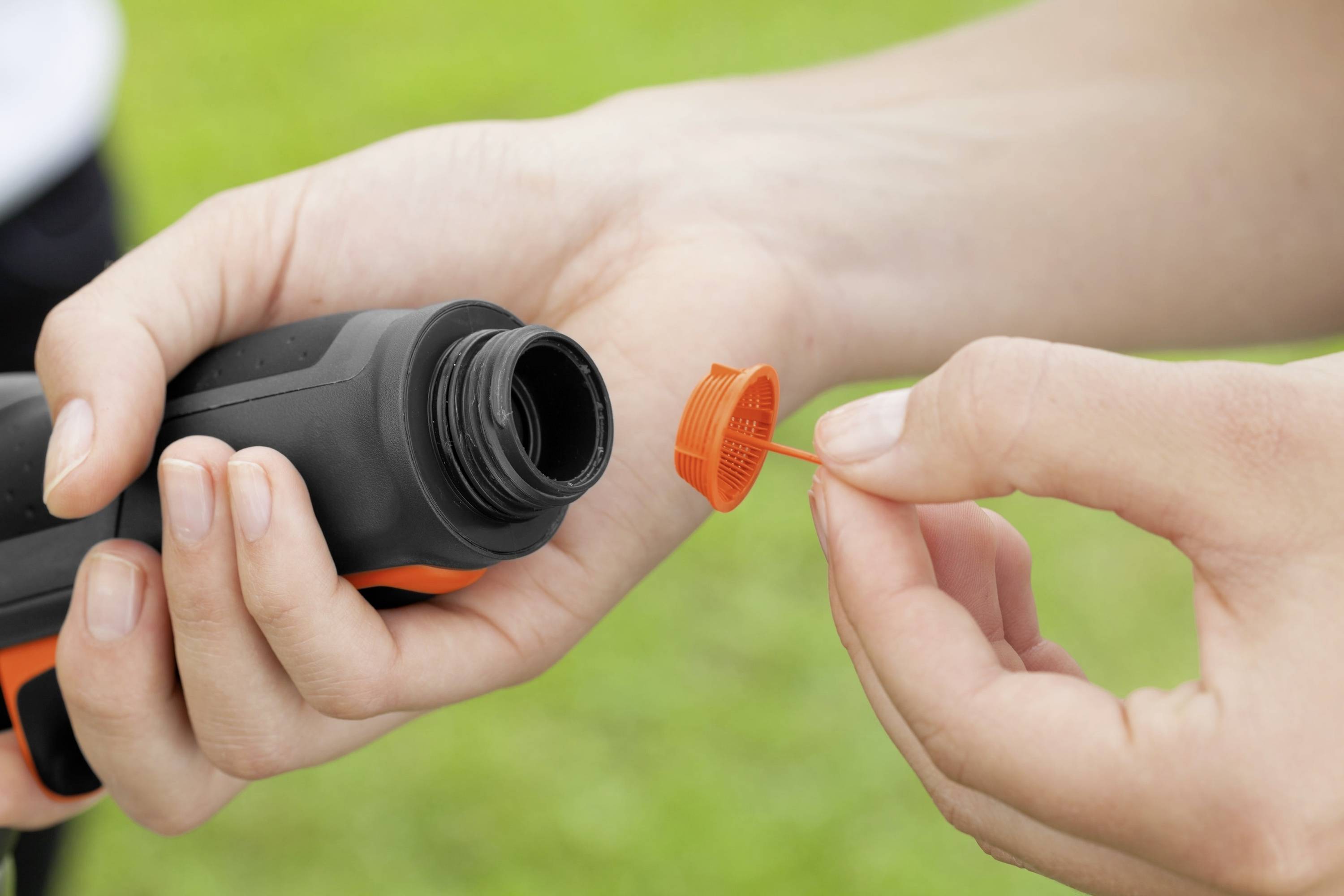 Une personne tient une bouteille avec un bouchon orange retiré dans un environnement verdoyant.