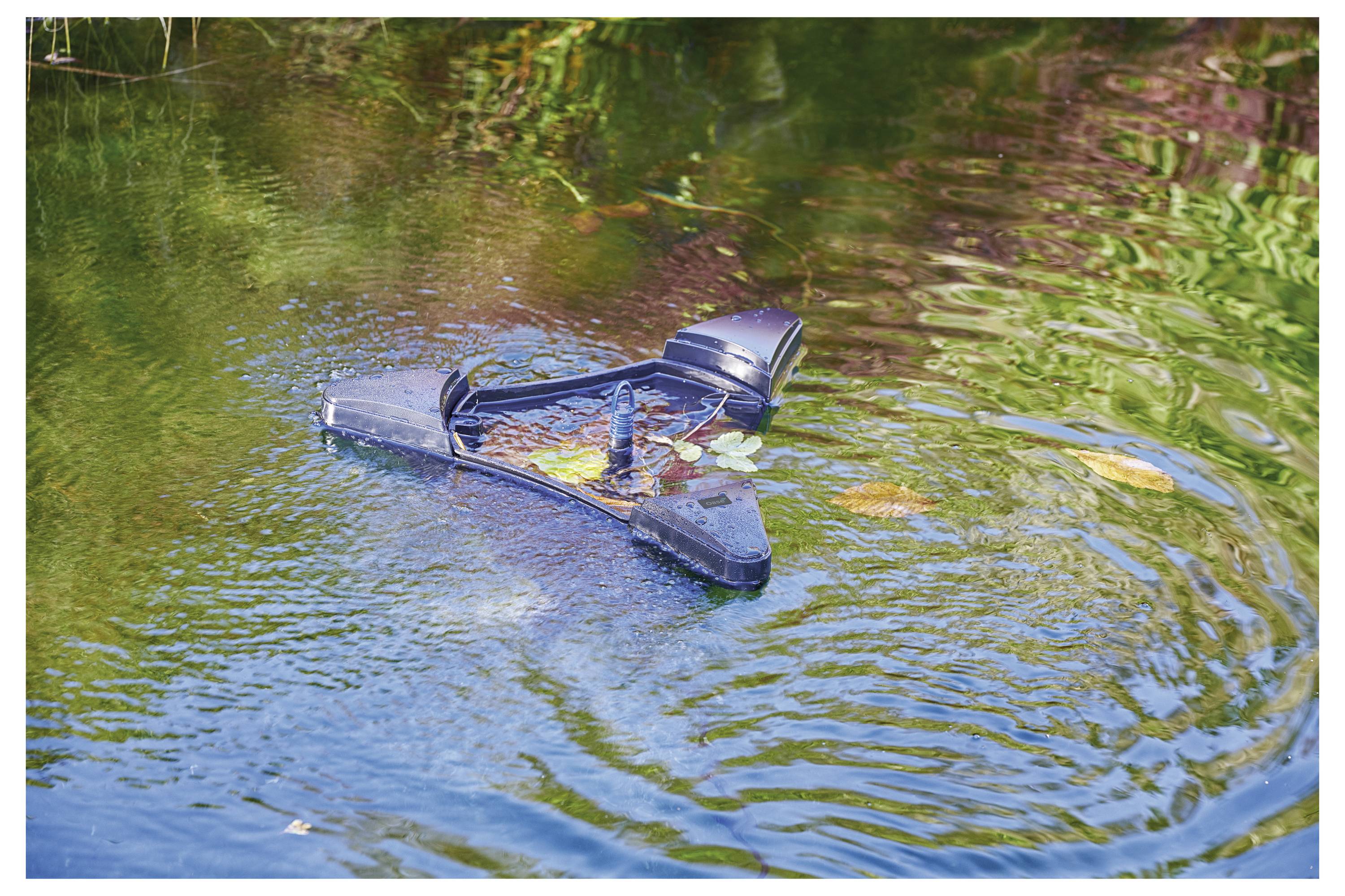Un rétroviseur cassé flotte sur un étang vert, à moitié submergé, entouré de rides et de petites taches d'algues et de plantes.