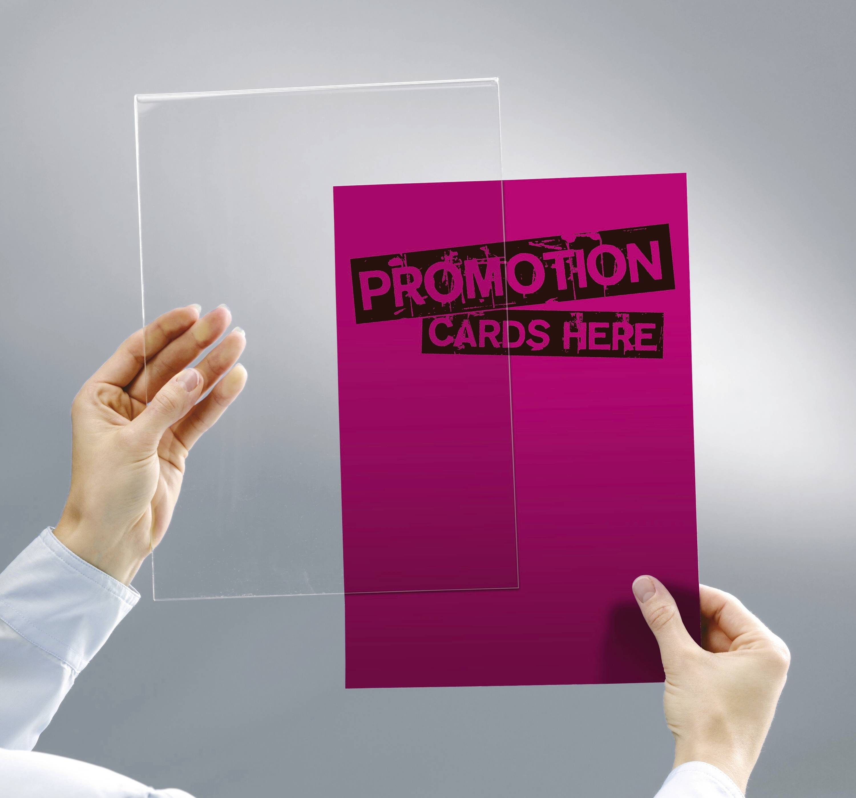 Une main tient une feuille transparente et une carte rose sur laquelle est inscrit le texte « Cartes de promotion ici » sur un fond gris.