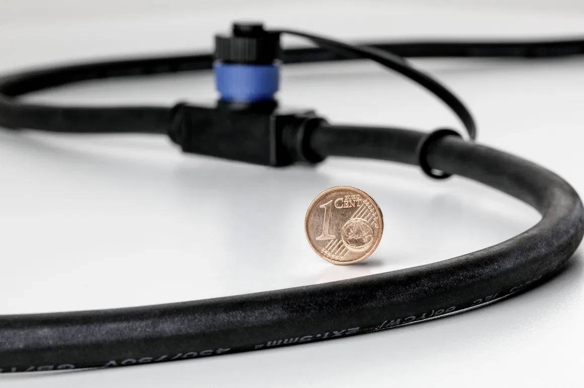 Une pièce de un centime se tient debout sur une table blanche, à côté d'un câble noir avec une fiche bleue en arrière-plan.