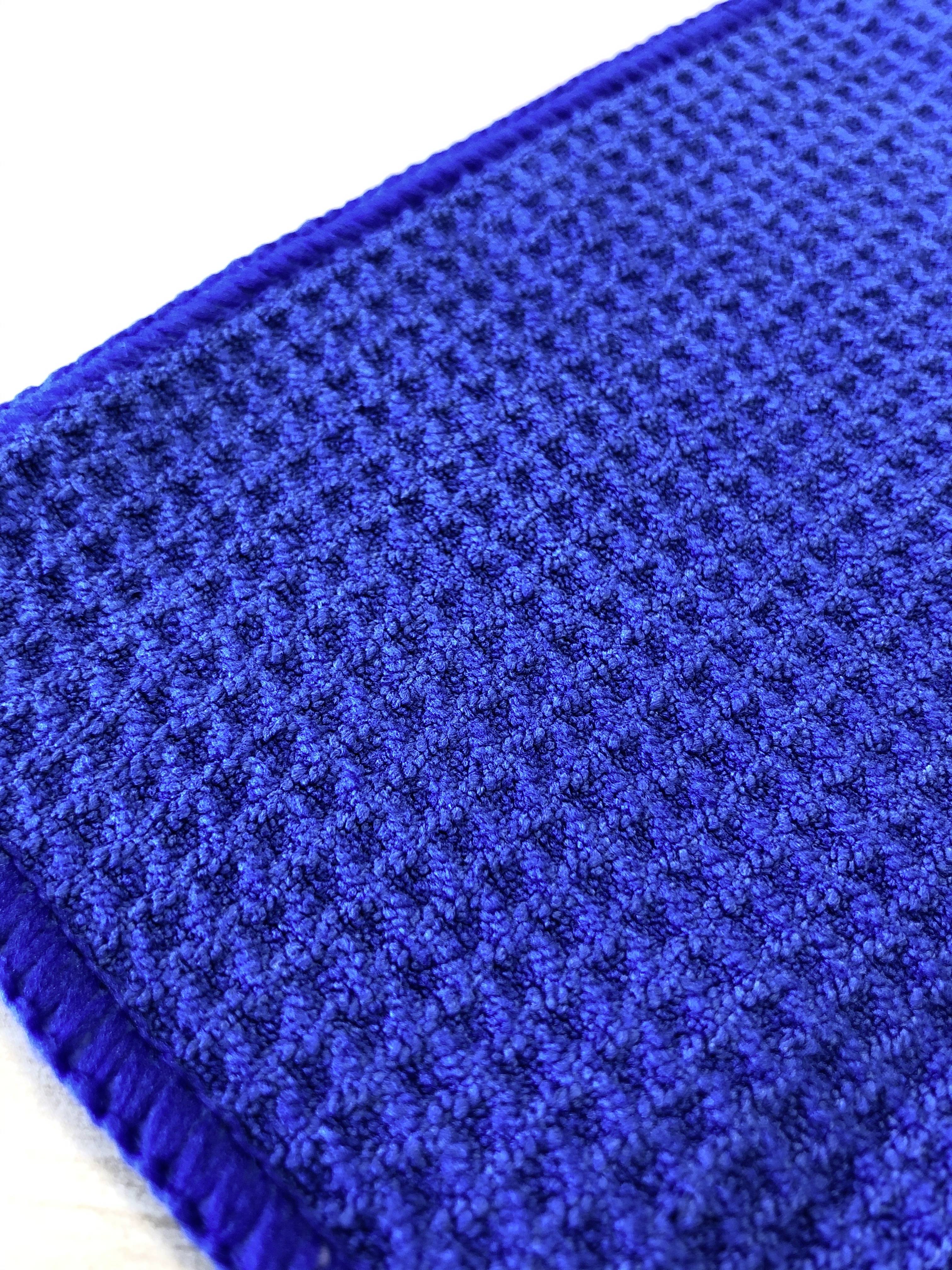 Un tissu bleu avec une texture de motif gaufré. Le tissu a une forme rectangulaire et repose sur une surface blanche.