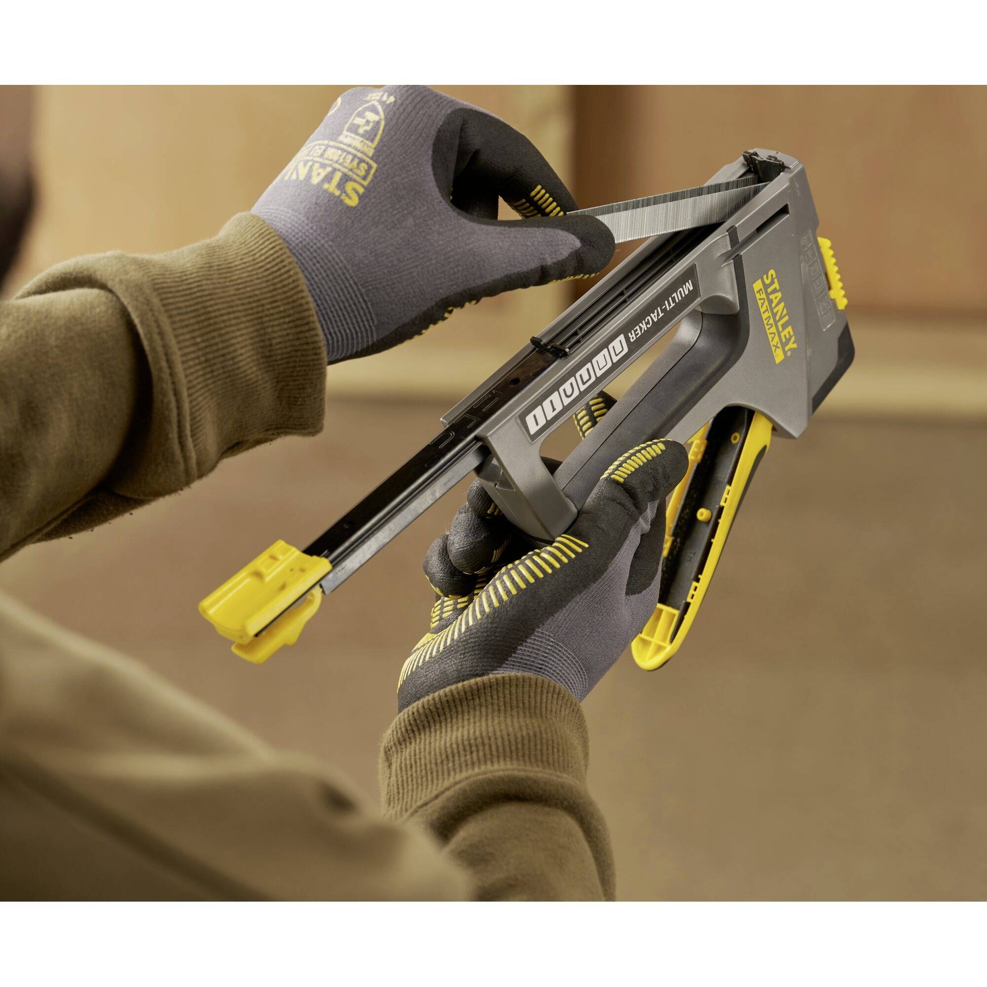 Une personne utilise un pistolet à agrafes jaune et gris pour charger des agrafes. Les gants offrent une protection pendant le travail.