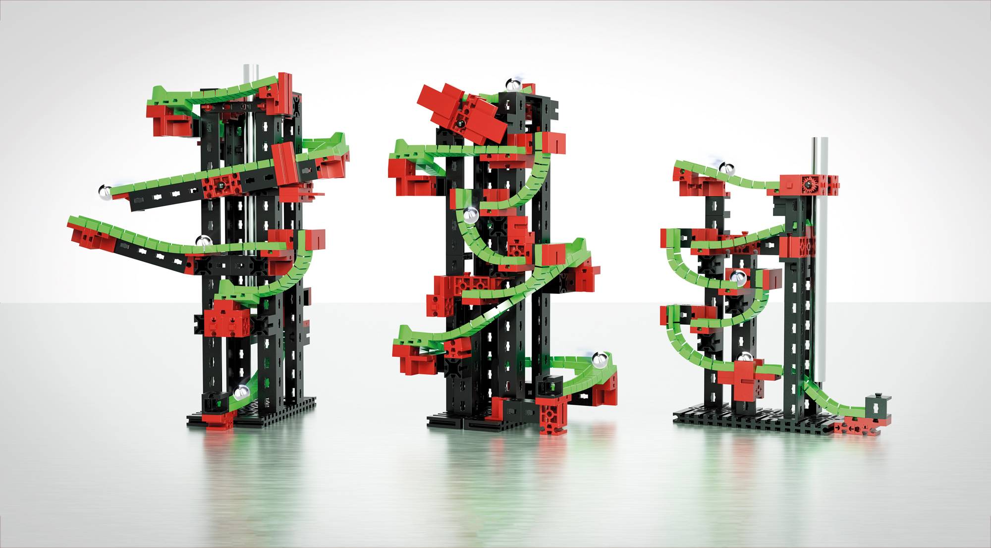 Trois tours de parcours de billes en spirale colorées, construites avec des blocs de construction comprenant des éléments rouges, verts et noirs, disposées sur une surface lisse.