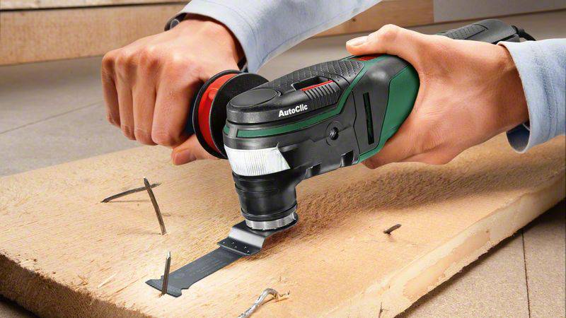 Une personne coupe des clous dans une poutre en bois à l'aide d'un outil multifonction oscillant.