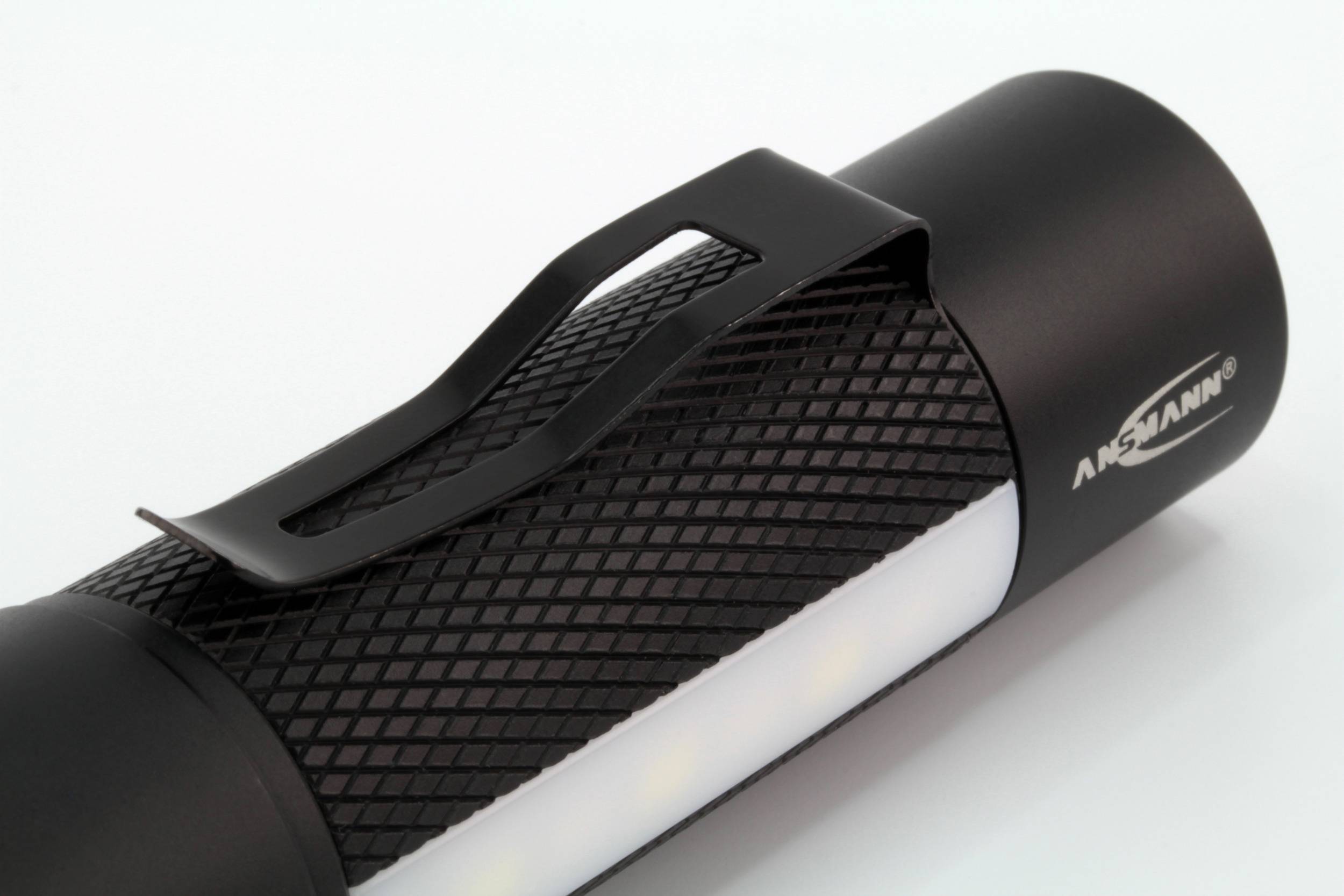 Lampe de poche noire avec clip, posée sur une surface blanche.
