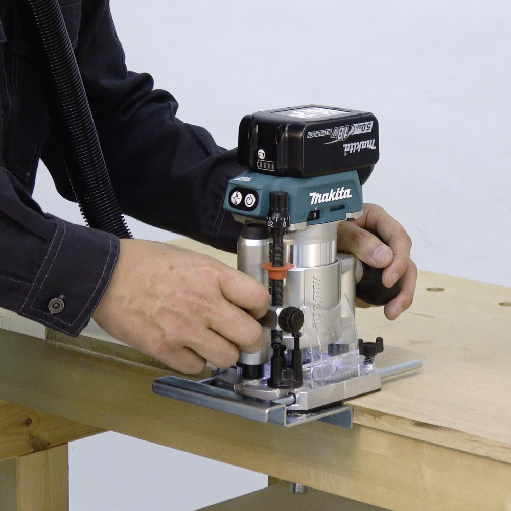 Une personne utilise une défonceuse électrique sur une table en bois. La machine est utilisée pour travailler précisément les surfaces en bois.