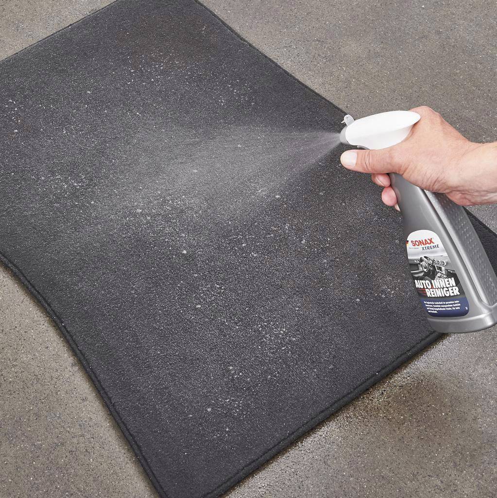 Une main vaporise un nettoyant intérieur de voiture sur un tapis noir à partir d'une bouteille afin d'éliminer les salissures.