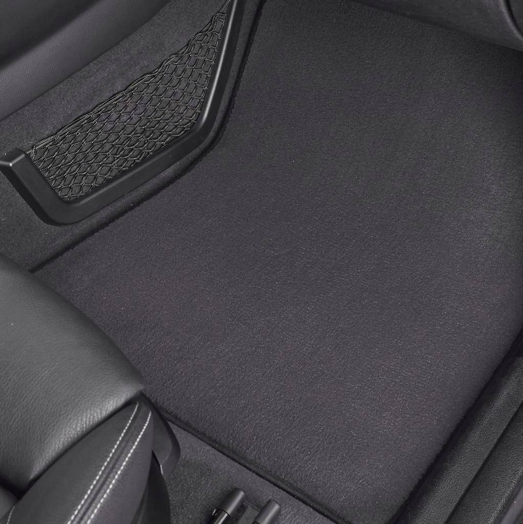 Intérieur d'une voiture avec un revêtement de sol noir et des sièges en cuir. Le sol est propre et montre les pédales au premier plan.