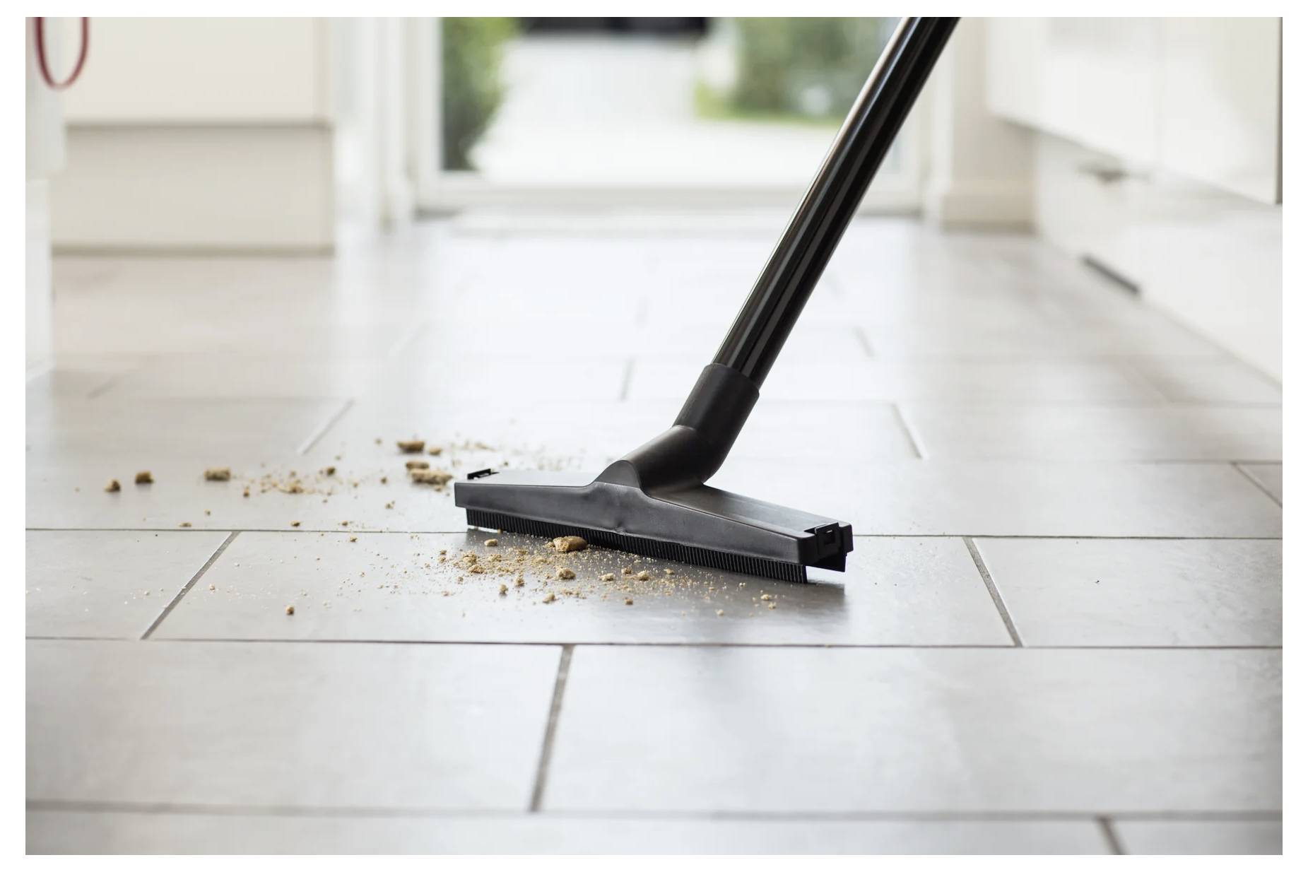 Un aspirateur nettoie des miettes sur un sol de cuisine carrelé, suggérant la propreté et l'ordre dans un environnement domestique.
