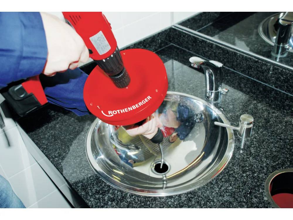 «Une personne utilisant un outil de plomberie Rothenberger rouge pour déboucher un lavabo de salle de bain.»