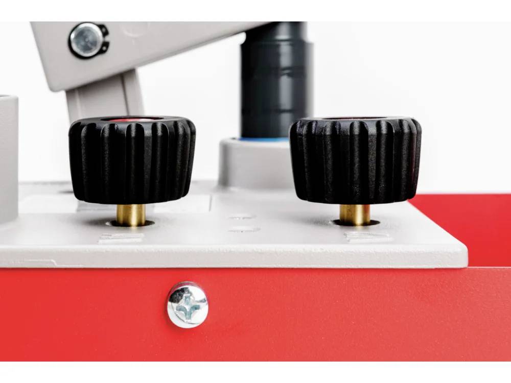 Image rapprochée de deux boutons de commande noirs sur une machine rouge et grise, indiquant un mécanisme permettant de régler ou de faire fonctionner un équipement.