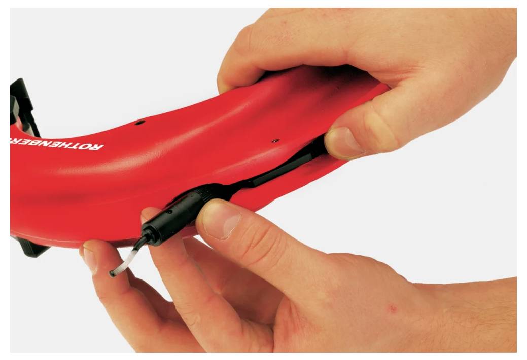 « L'illustration « Insertion du joint en caoutchouc pour couvrir le port de charge » montre des mains installant un joint de protection dans un appareil en plastique rouge. »