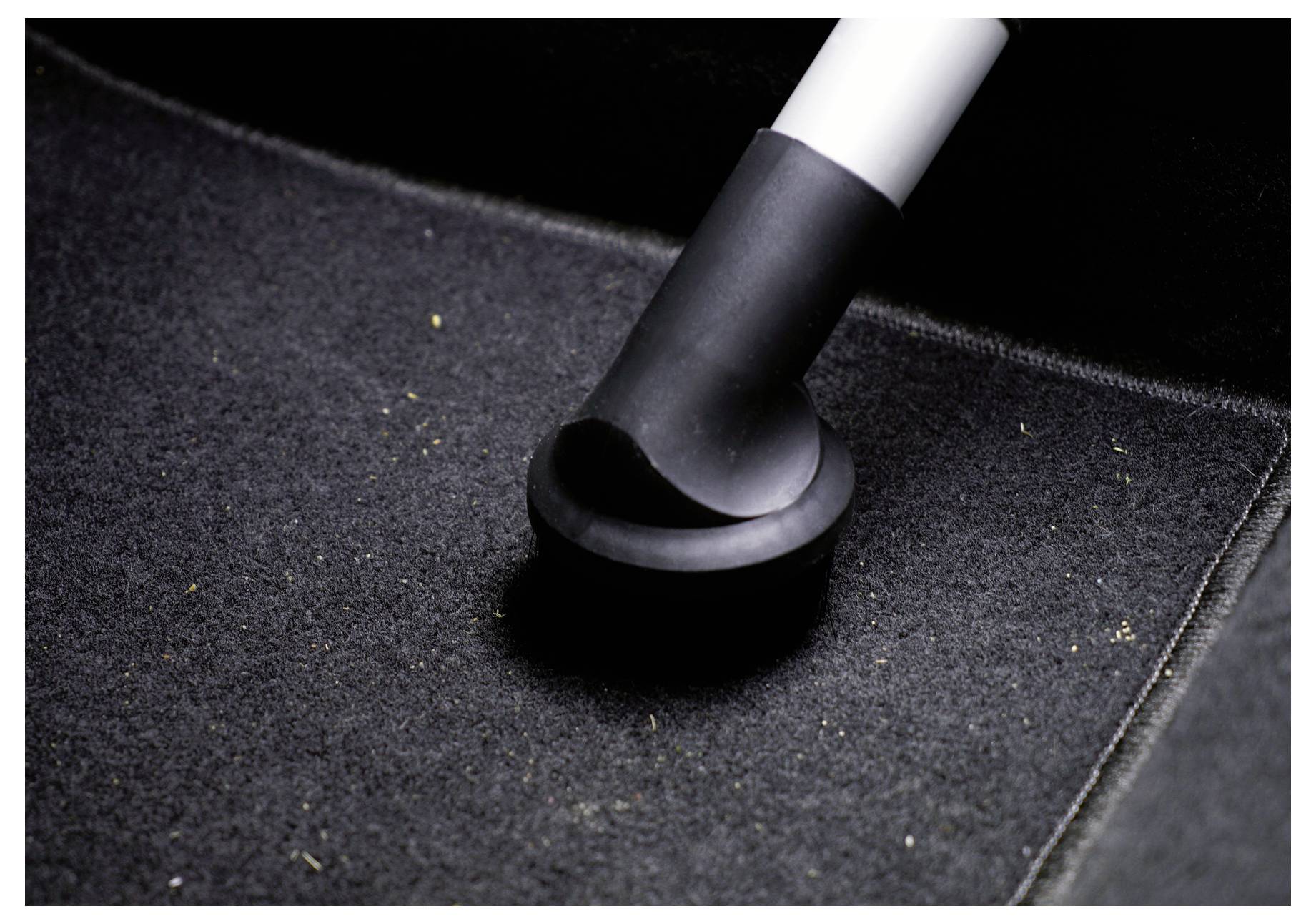 Gros plan d'une brosse d'aspirateur nettoyant un tapis ou un paillasson foncé, éliminant la poussière et les débris.
