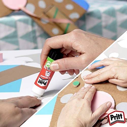 Des mains utilisant un stick de colle Pritt et fixant un morceau de papier rose circulaire sur une feuille de carton, avec des matériaux de bricolage en arrière-plan.