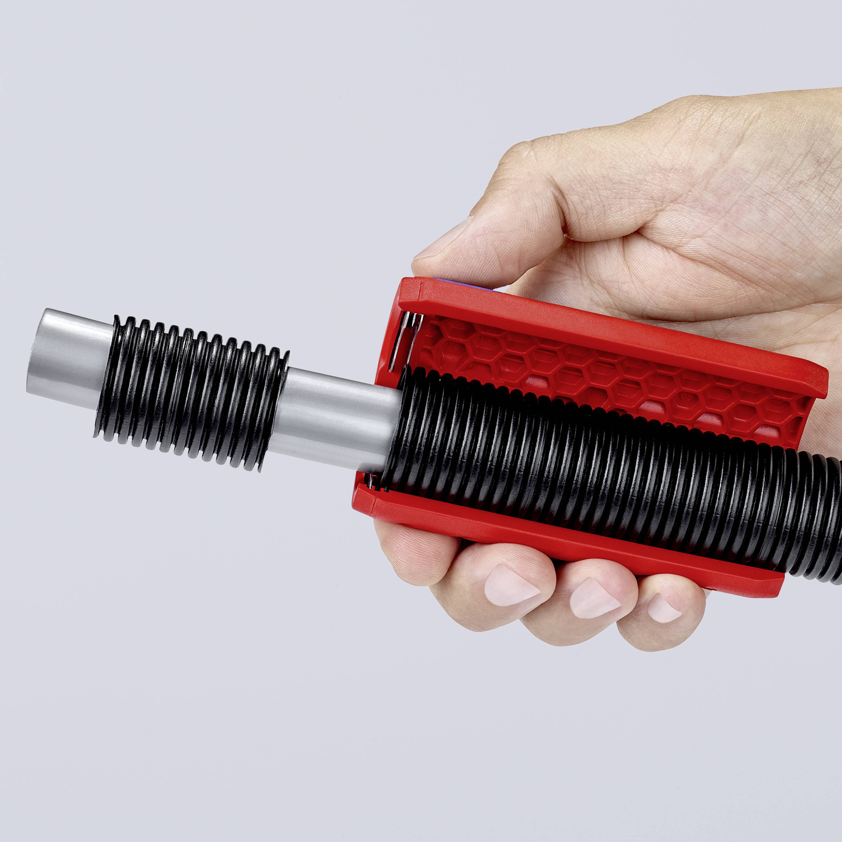 Une main tient un outil de préhension rouge avec un ressort spiral noir sur un fond gris.