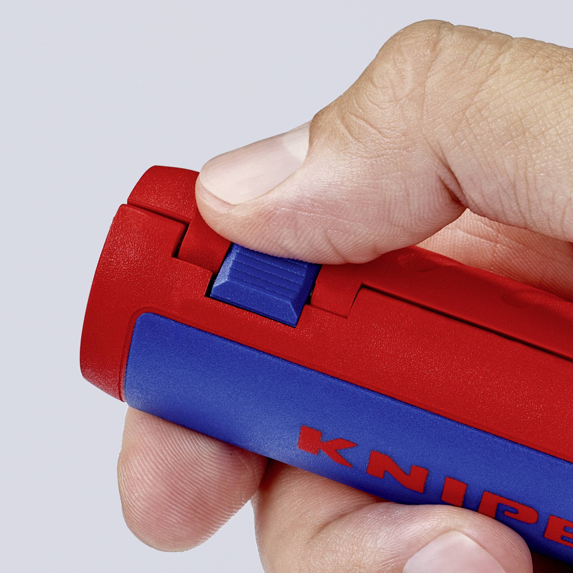 Une main actionne le curseur d'un cutter universel rouge, le préparant pour utilisation.