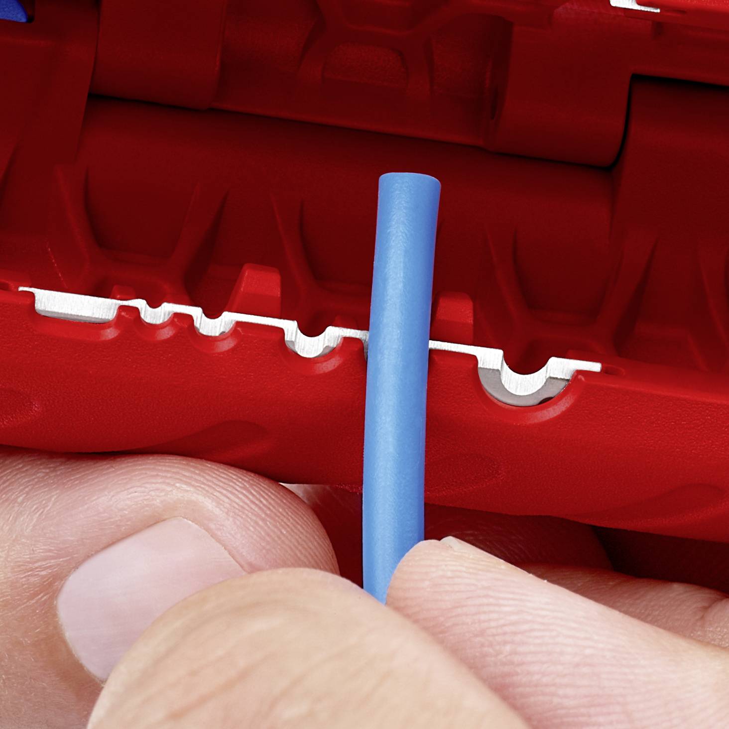 Deux mains tiennent un câble bleu devant un outil rouge et blanc utilisé pour dénuder les câbles.