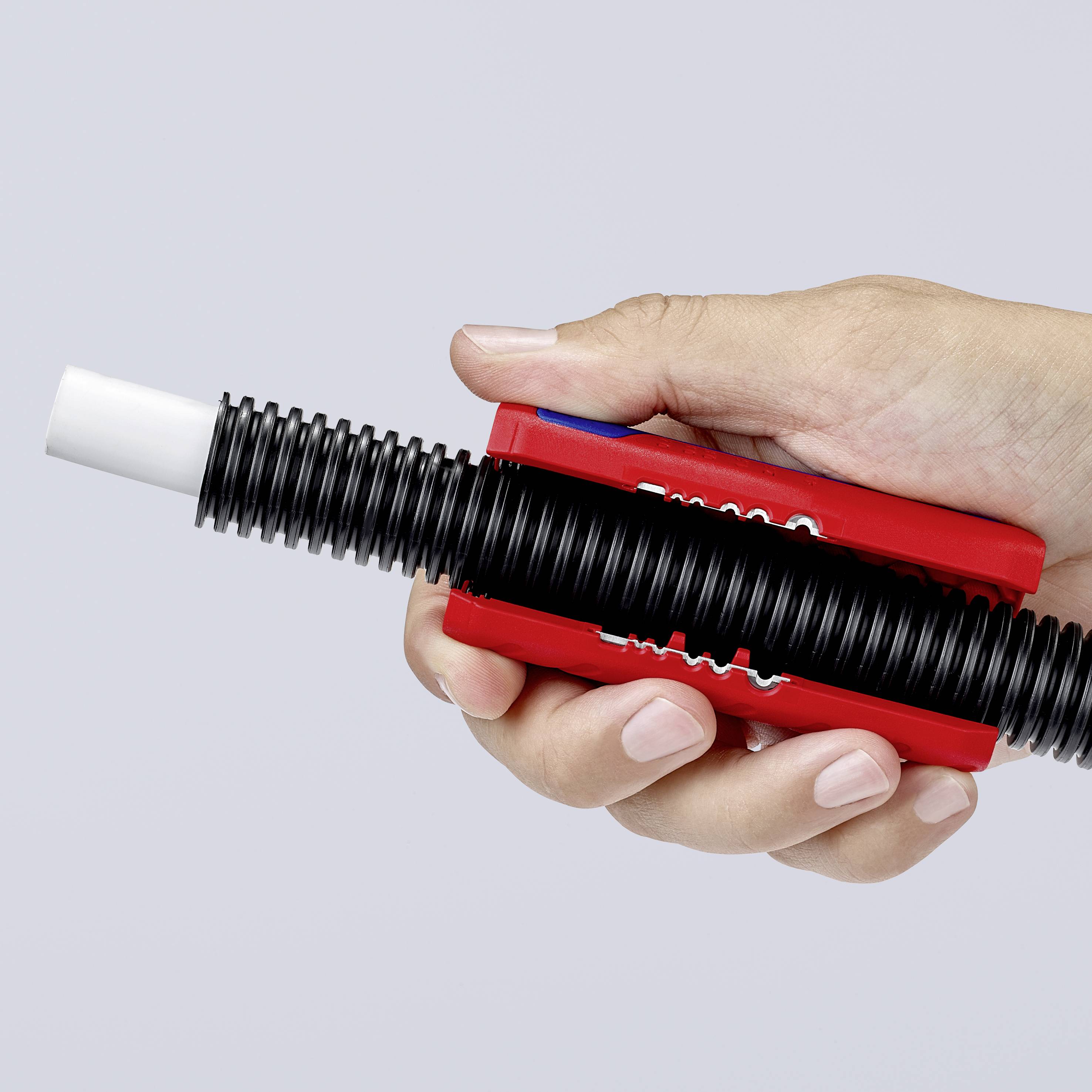 Une main tient un outil de tuyauterie rouge avec une ouverture striée noire, adapté pour connecter ou sceller des tuyaux.