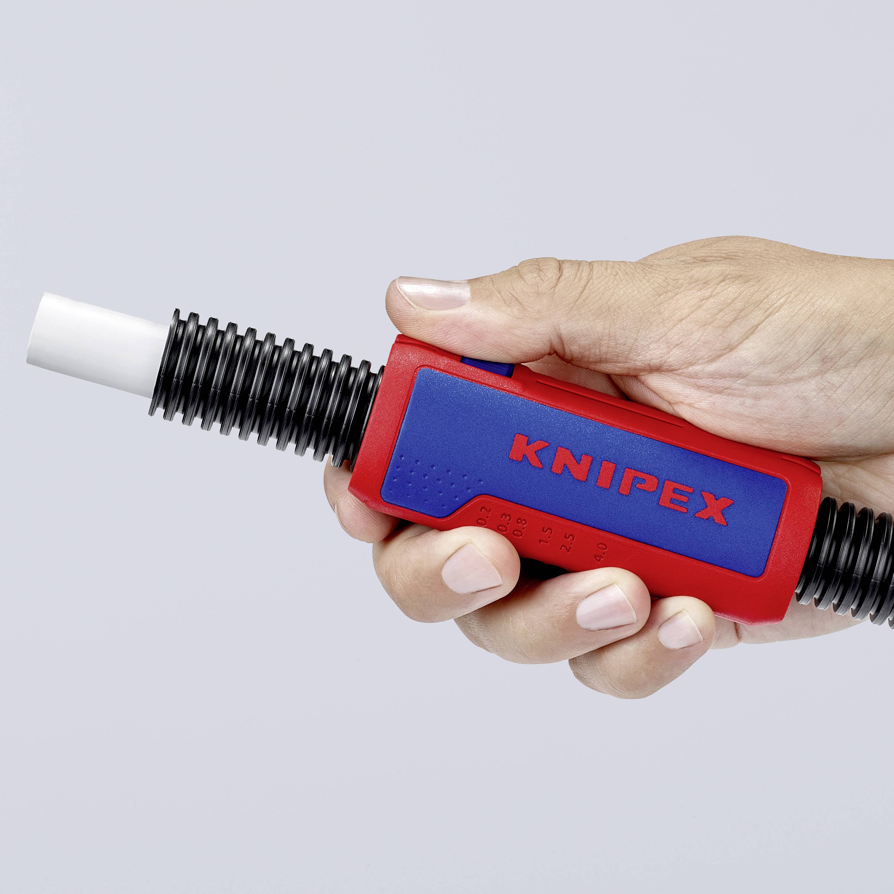 Une main tient un décapant rouge de la marque KNIPEX. L'outil dispose d'un embout en plastique noir et est utilisé pour les travaux de câblage.