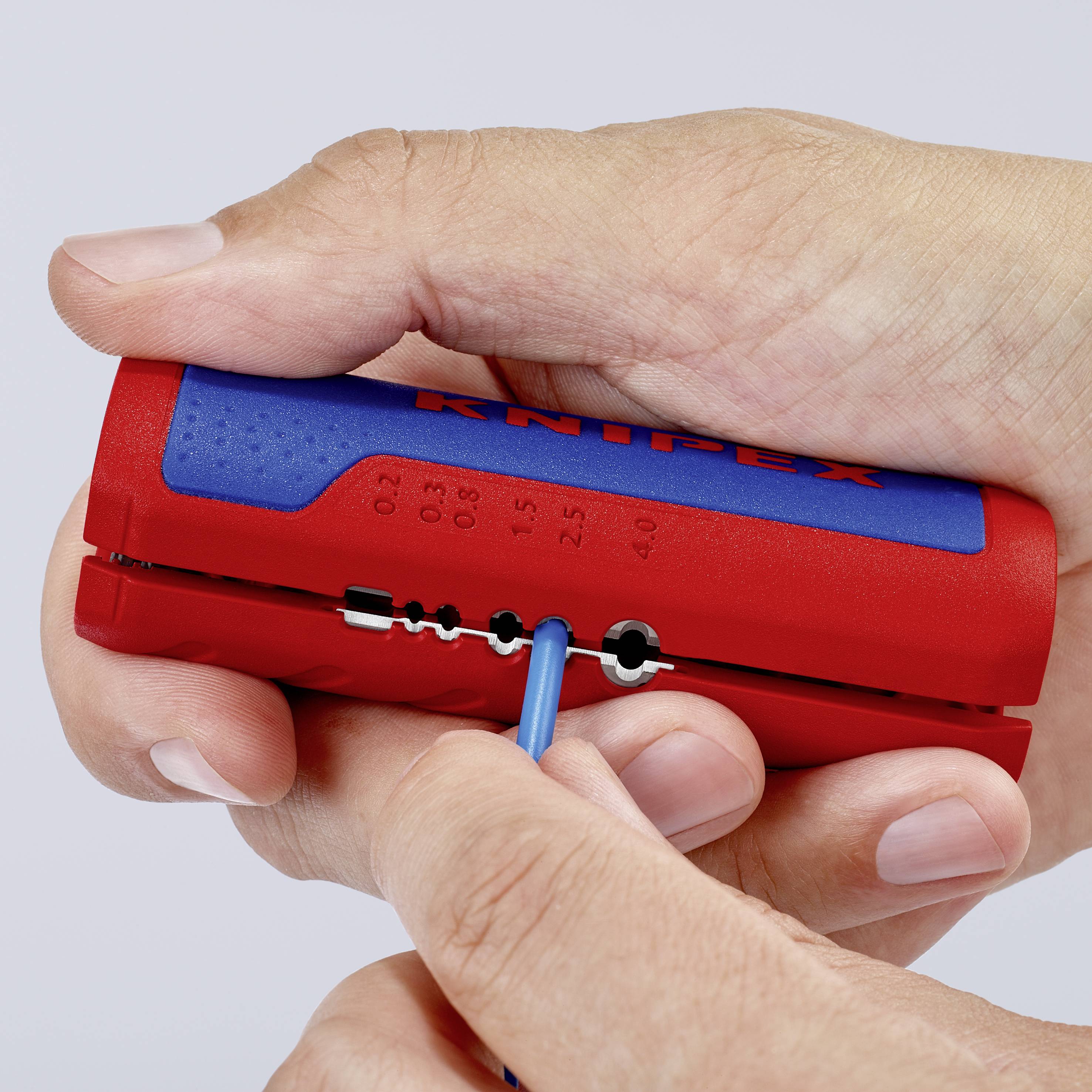 Une personne utilise un outil rouge et bleu pour dénuder des câbles de différentes épaisseurs.