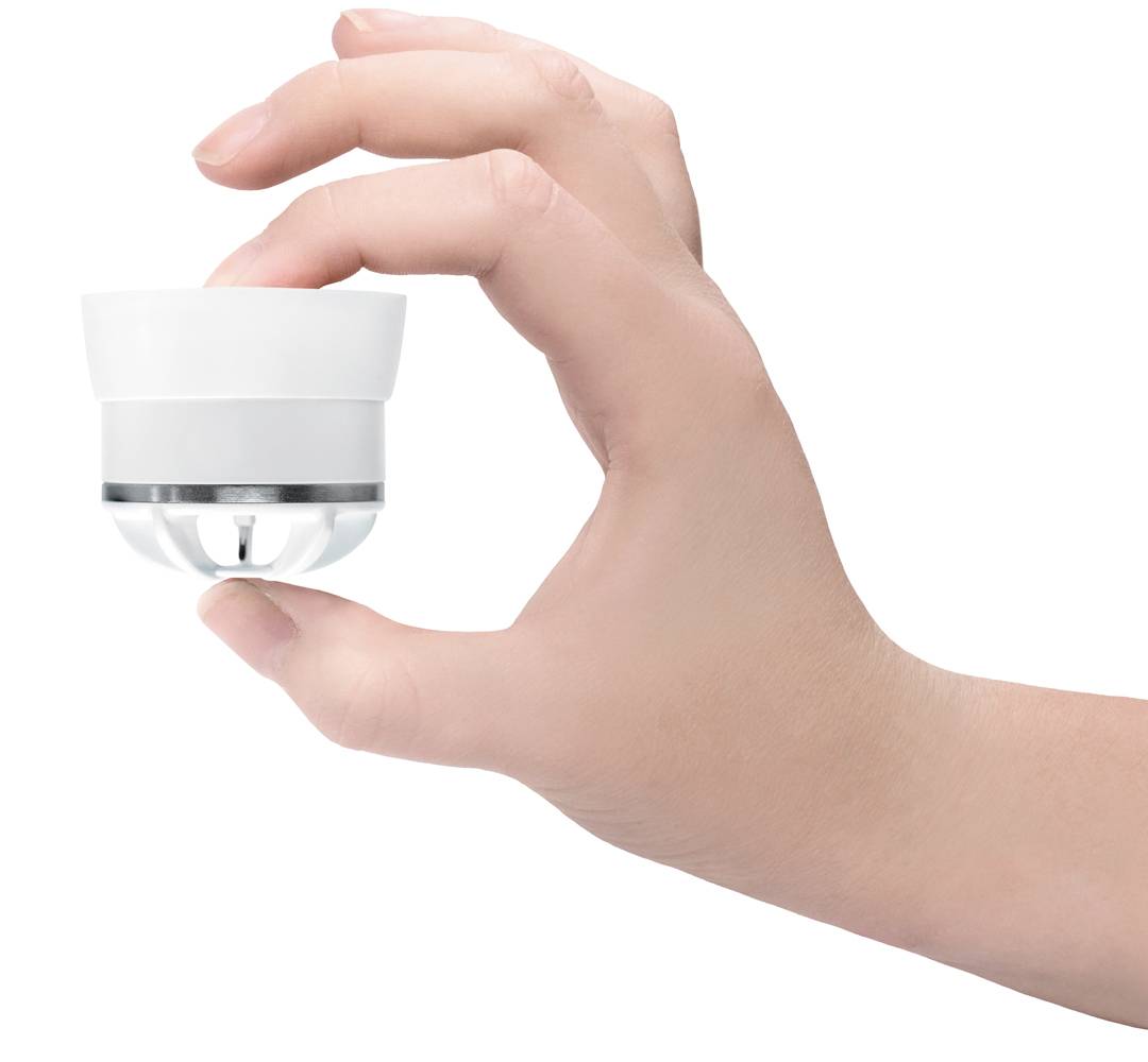 Une main tient une petite caméra de surveillance blanche. La caméra est ronde et possède un objectif brillant.