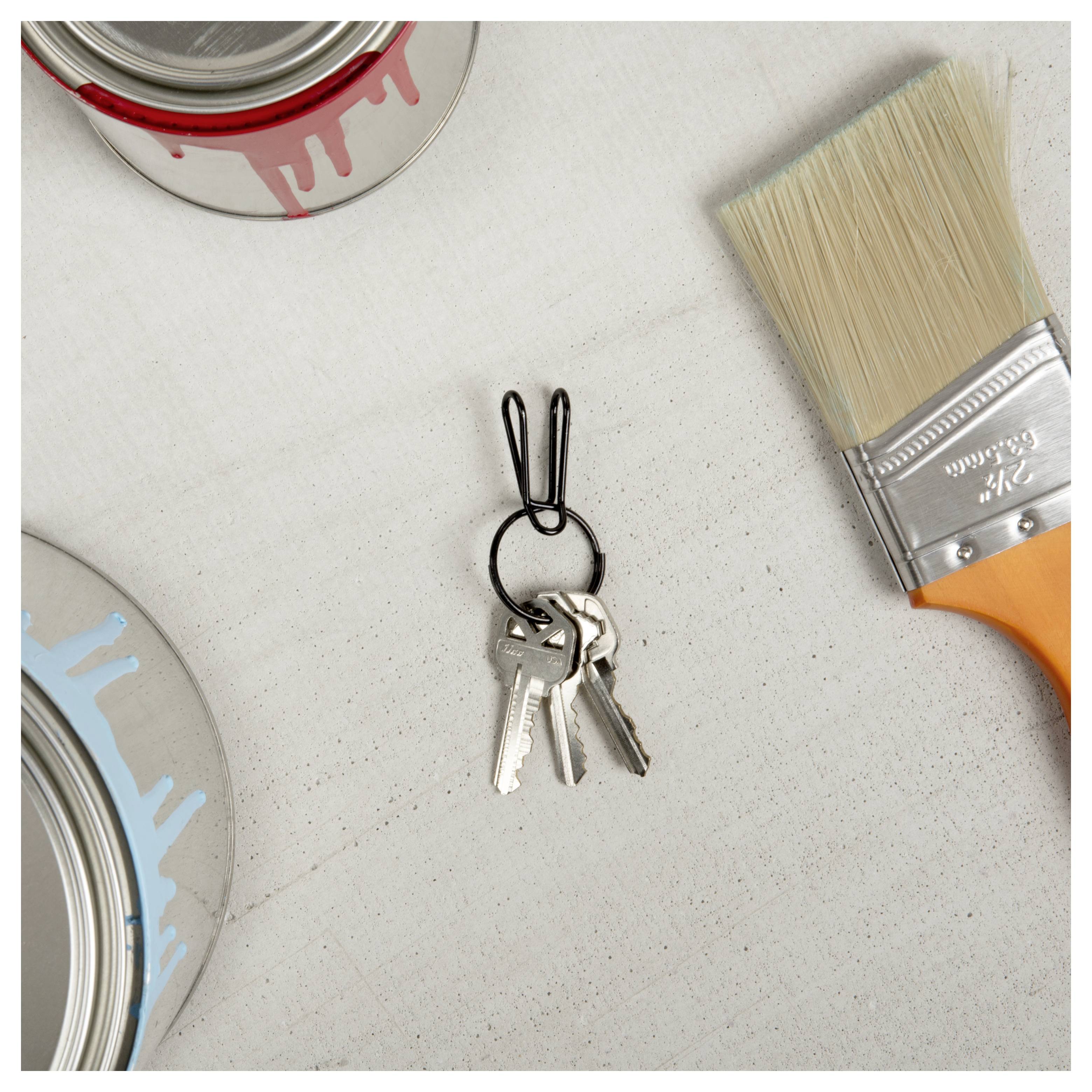 Un ensemble de clés avec un porte-clés en forme de lapin est posé sur une table, entouré de boîtes de peinture partiellement ouvertes avec des gouttes rouges et bleues et un pinceau.