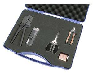 Une valise ouverte contenant des outils : une pince à sertir, un coupe-câble, des ciseaux, et un petit appareil rectangulaire, tous soigneusement enchâssés dans de la mousse.
