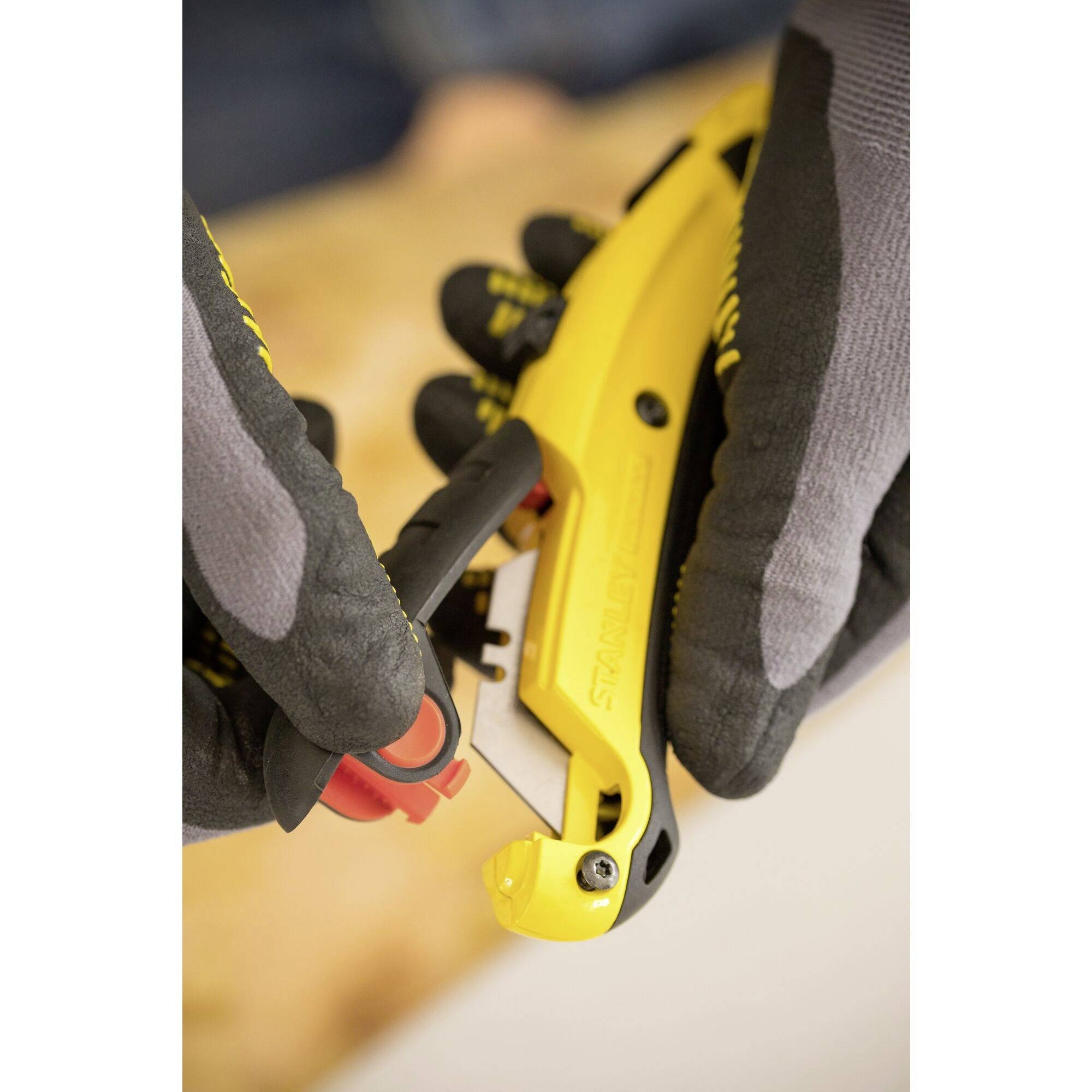 Une personne portant des gants gris tient un couteau de sécurité jaune et change la lame.