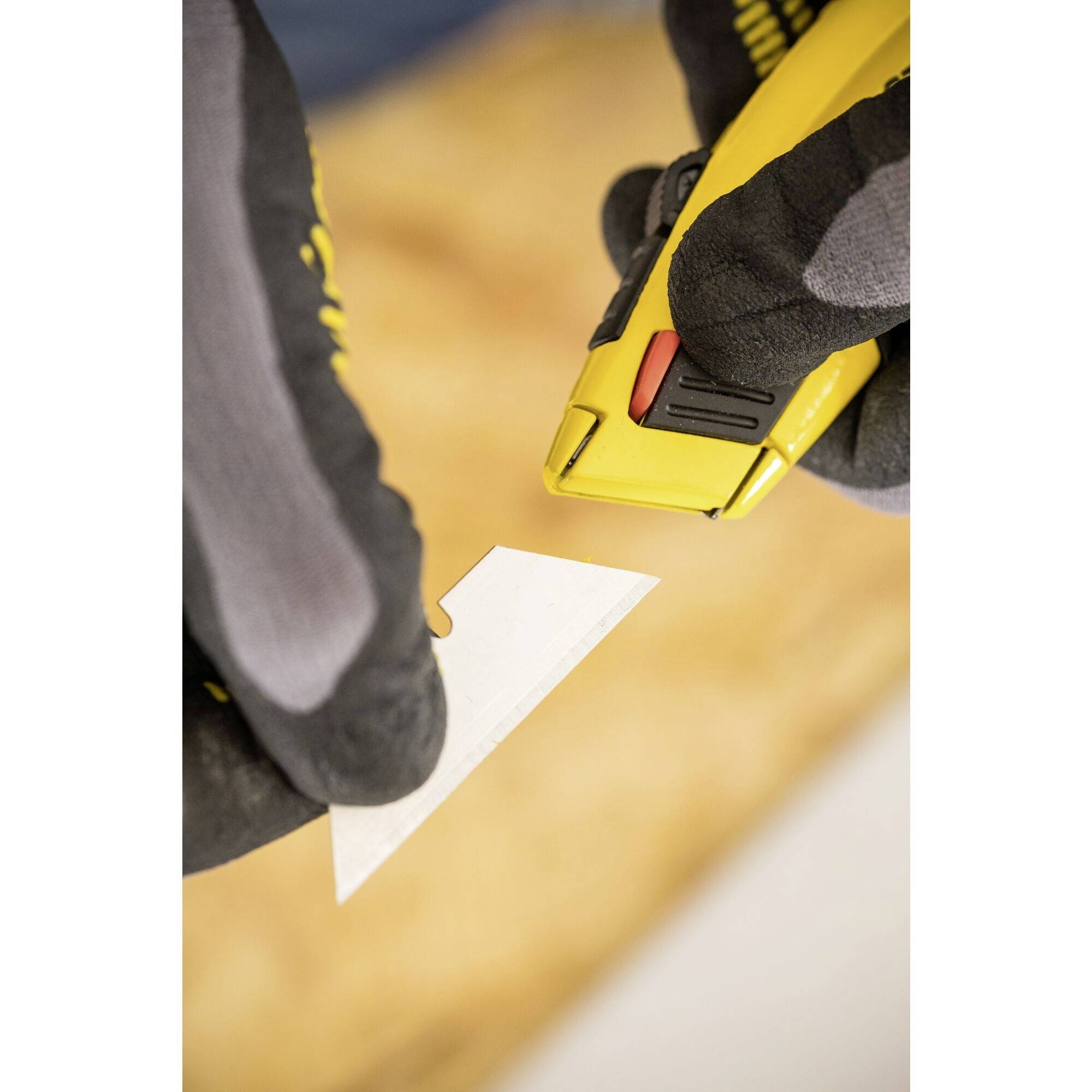 Une personne fait glisser un outil de coupe jaune sur une surface blanche de découpe, avec un fond en bois flou.