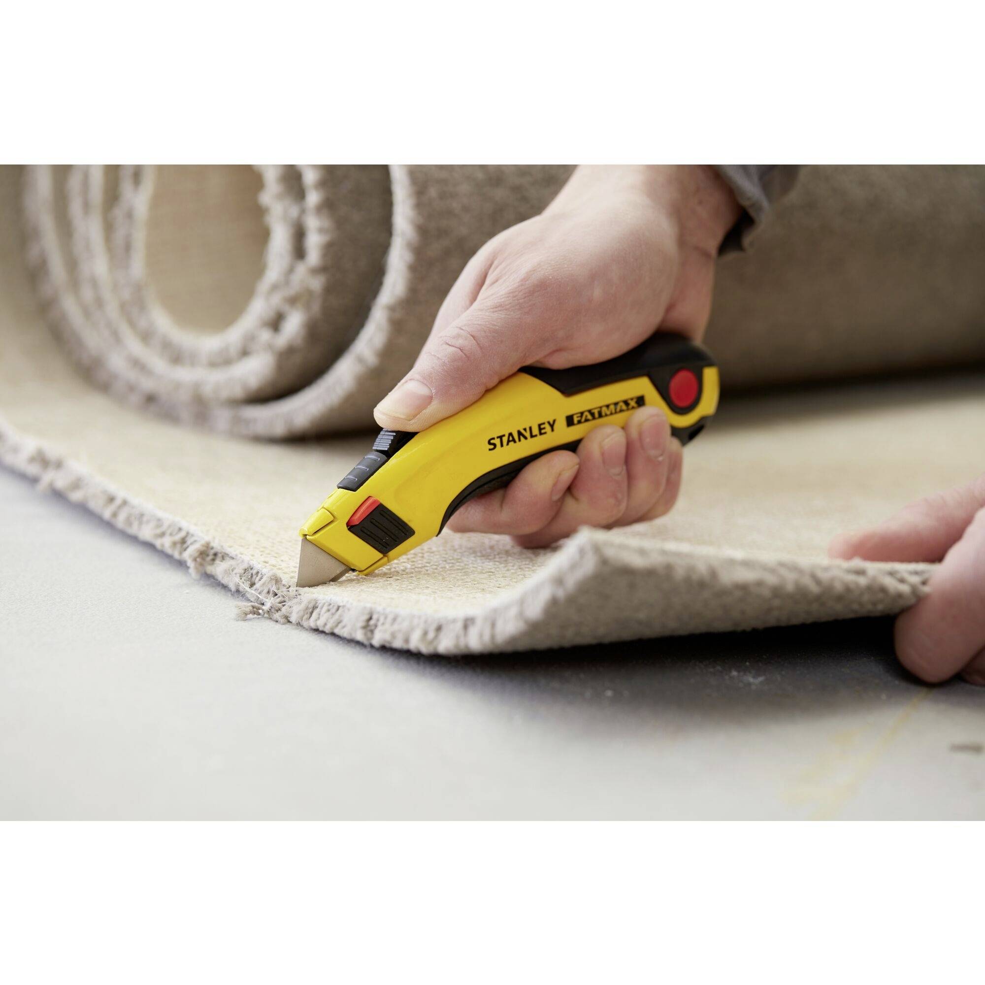 Une personne coupe un morceau de tapis avec un cutter jaune. Le tapis est enroulé et placé sur un sol.