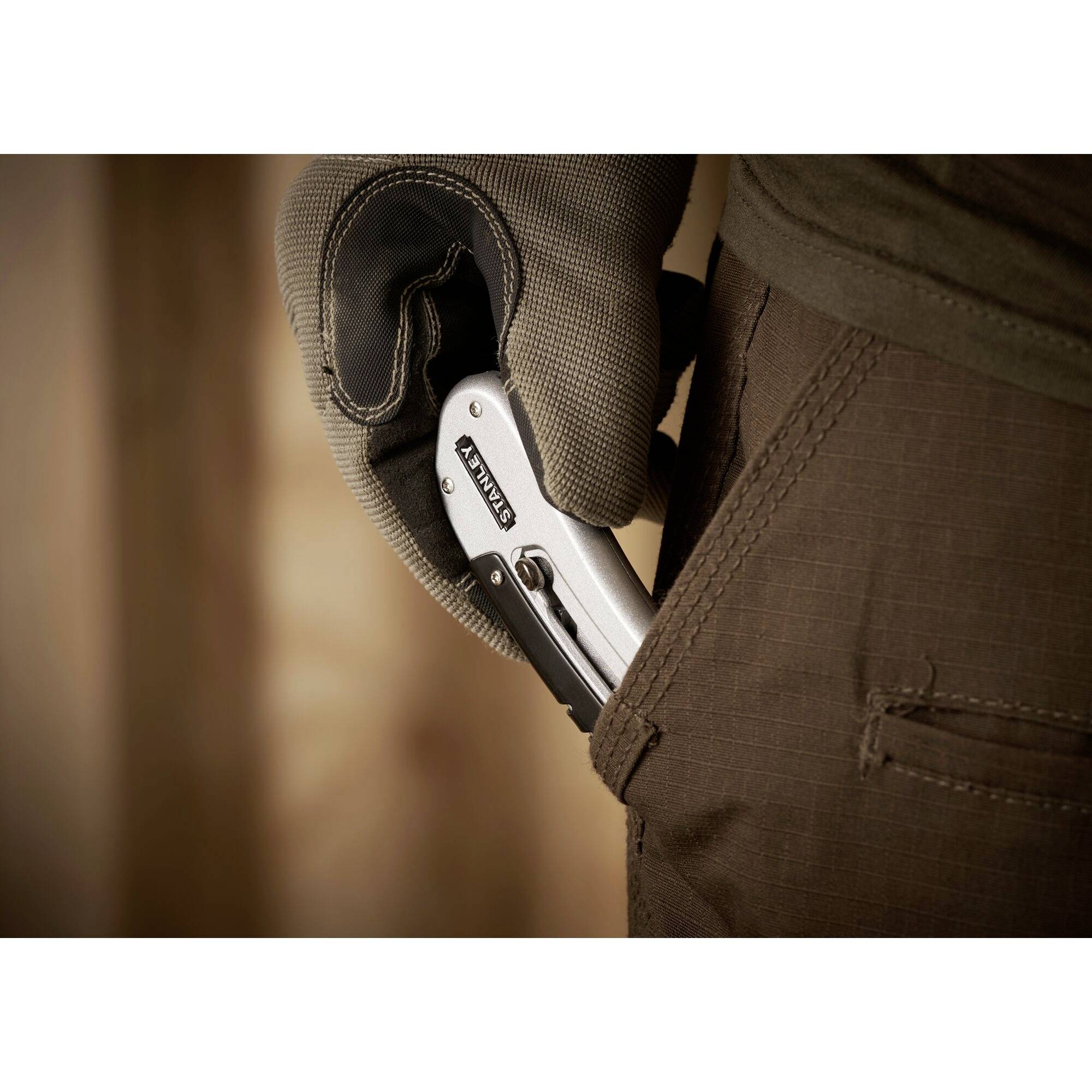 Une main gantée glisse un outil multifonction pliable dans la poche de pantalon.