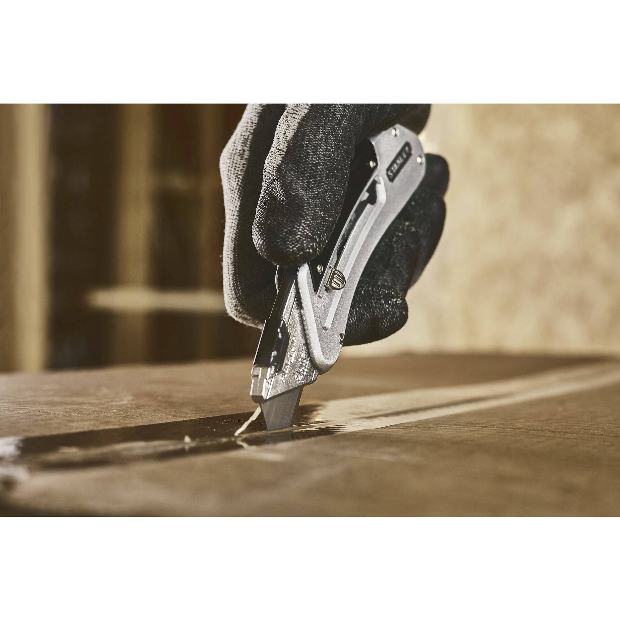 Une main gantée coupe un carton avec un couteau utilitaire. Le couteau se déplace le long d'une ligne droite.