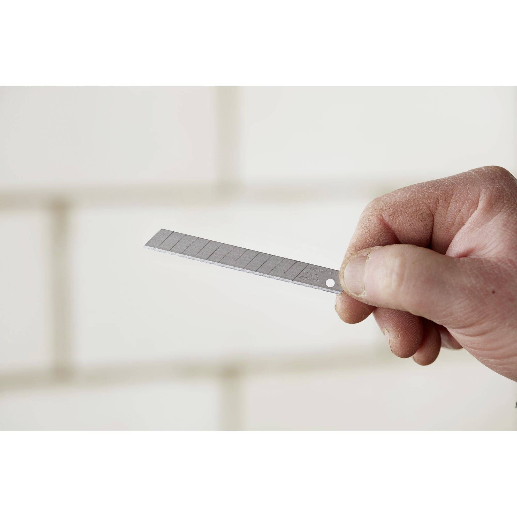 Une main tient un couteau à lame rétractable en l'air, prête à couper ou à bricoler. L'arrière-plan est flou.