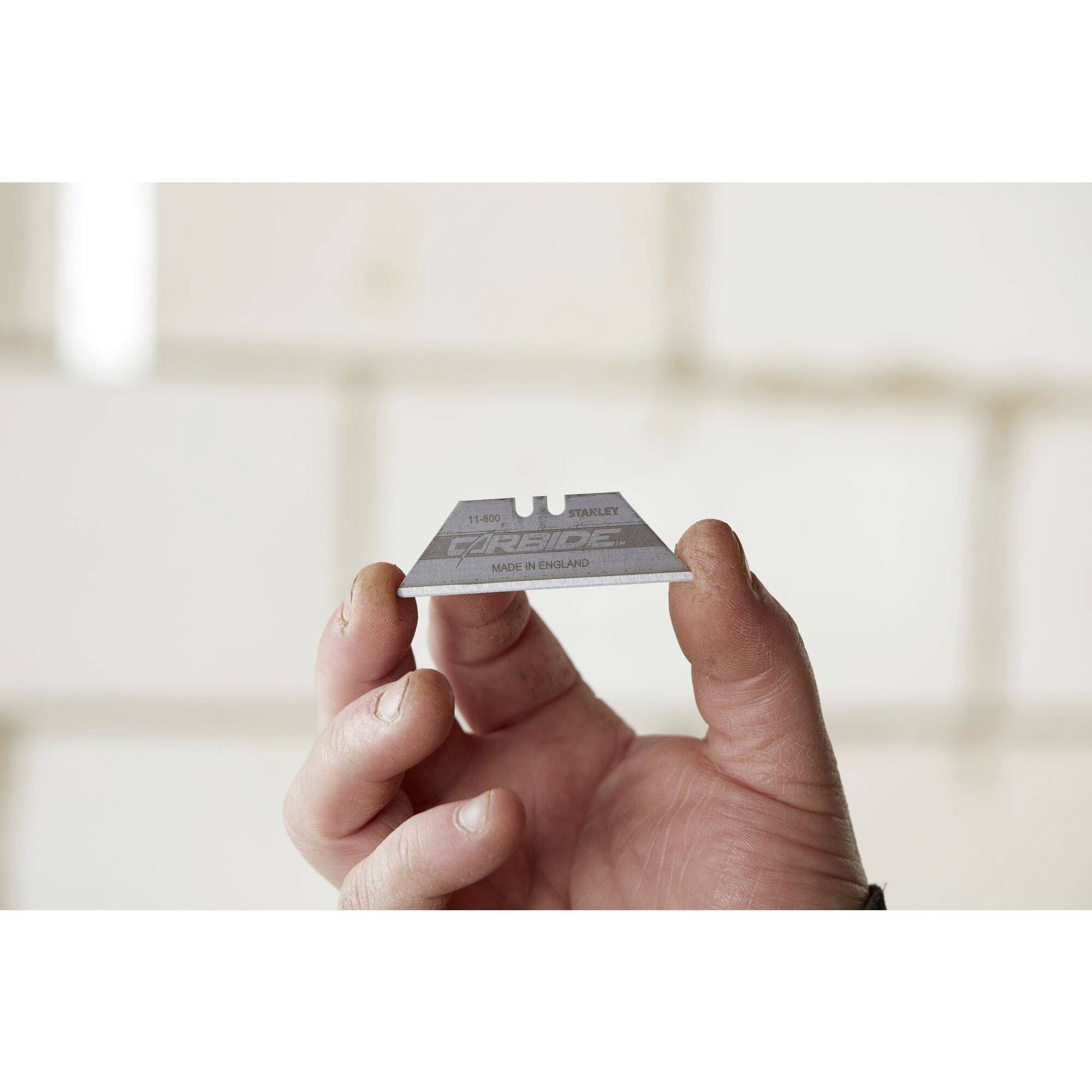 Gros plan d'une main tenant une lame de rasoir tranchante portant l'inscription 