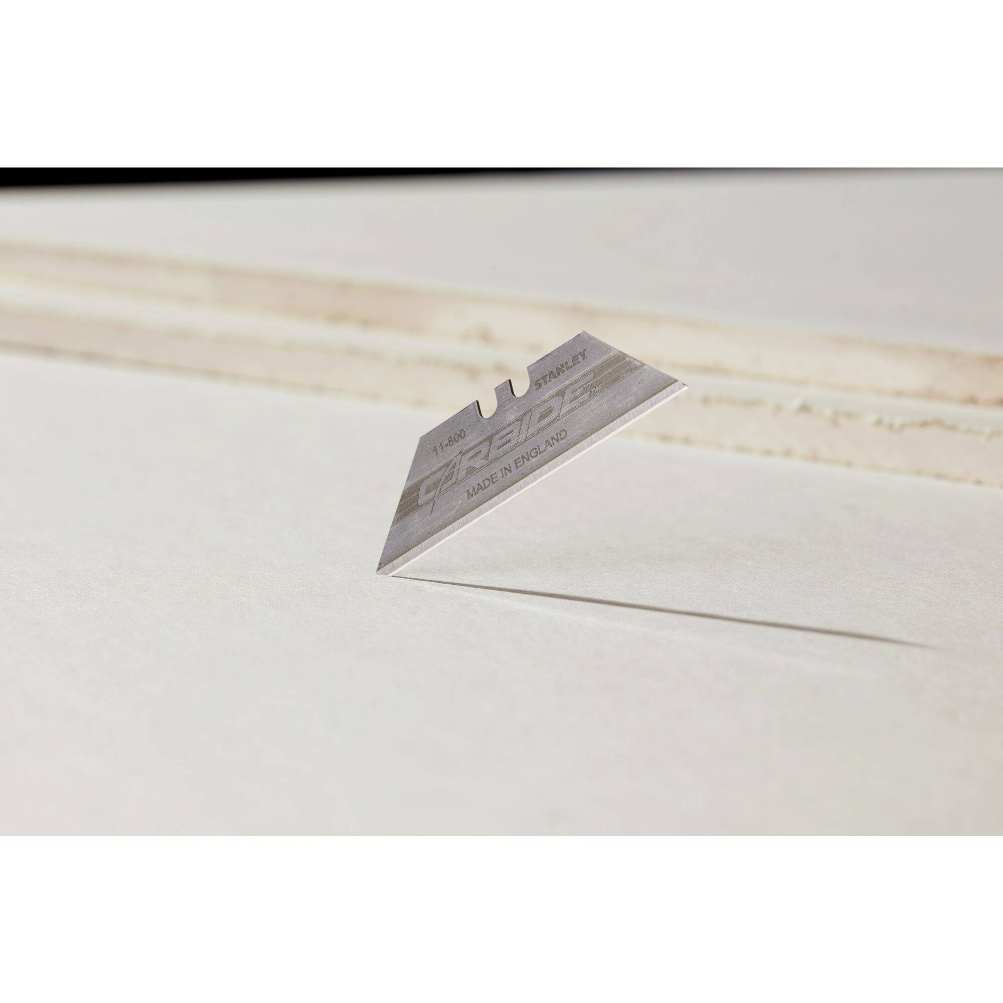 Une lame de rasoir unique flotte au-dessus d'une surface, projetant une ombre nette. L'arrière-plan est flou et lumineux.