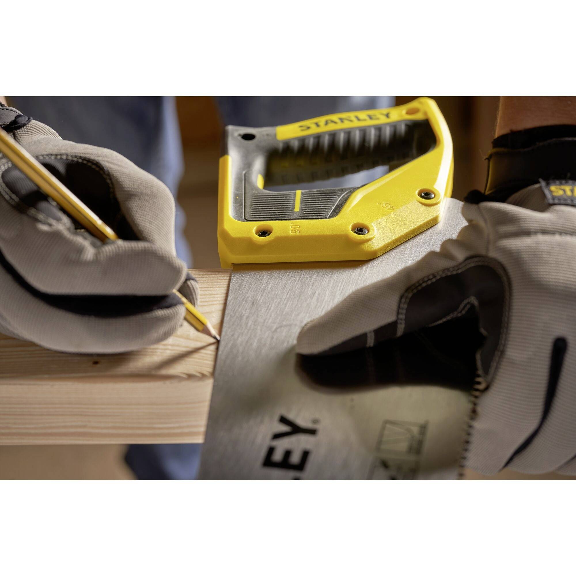 Une personne portant des gants marque un morceau de bois avec un crayon et une équerre jaune, puis le scie.