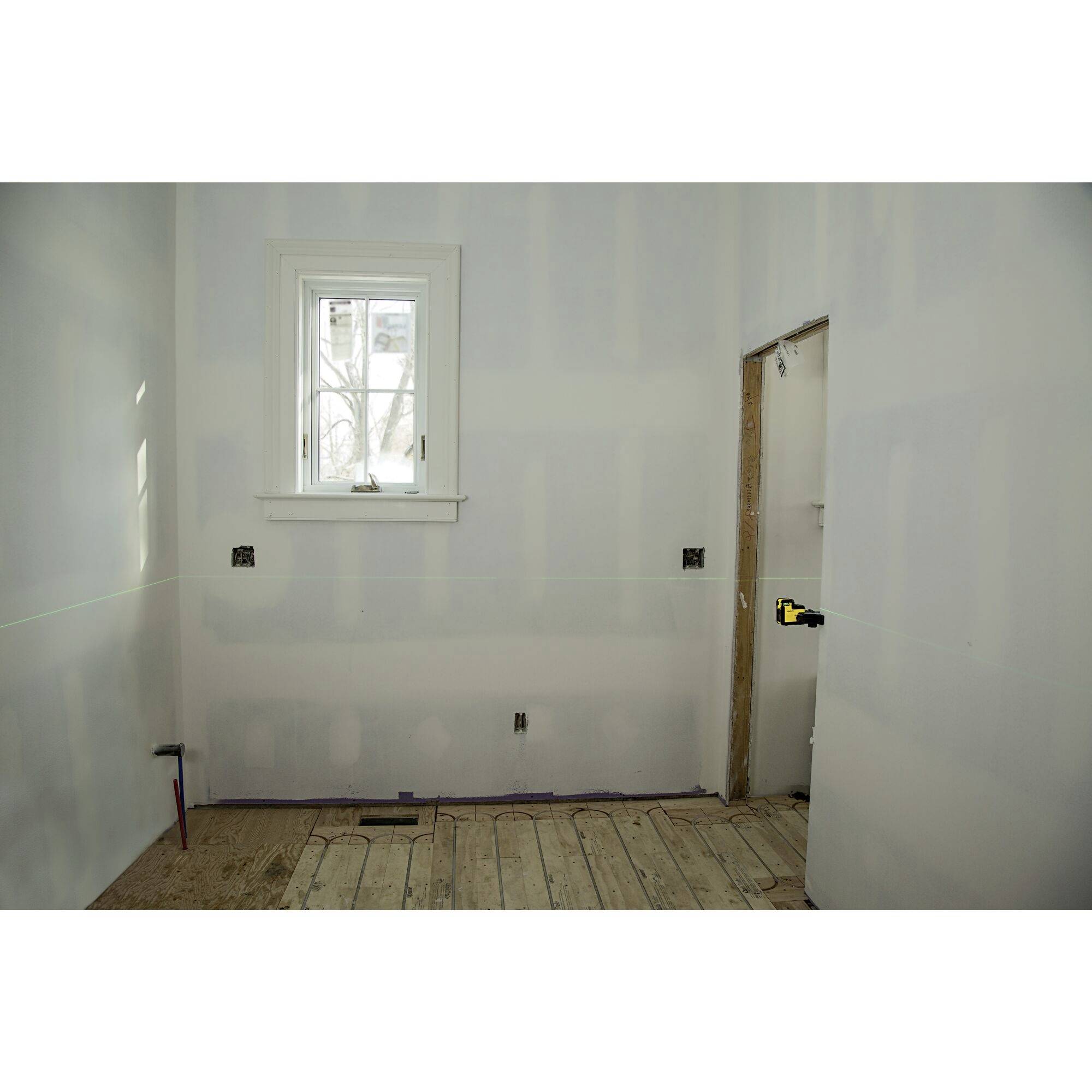 Un espace vide avec un sol en bois, des murs peints en blanc, une fenêtre et une ouverture de porte inachevée. La pièce semble en cours d'aménagement.