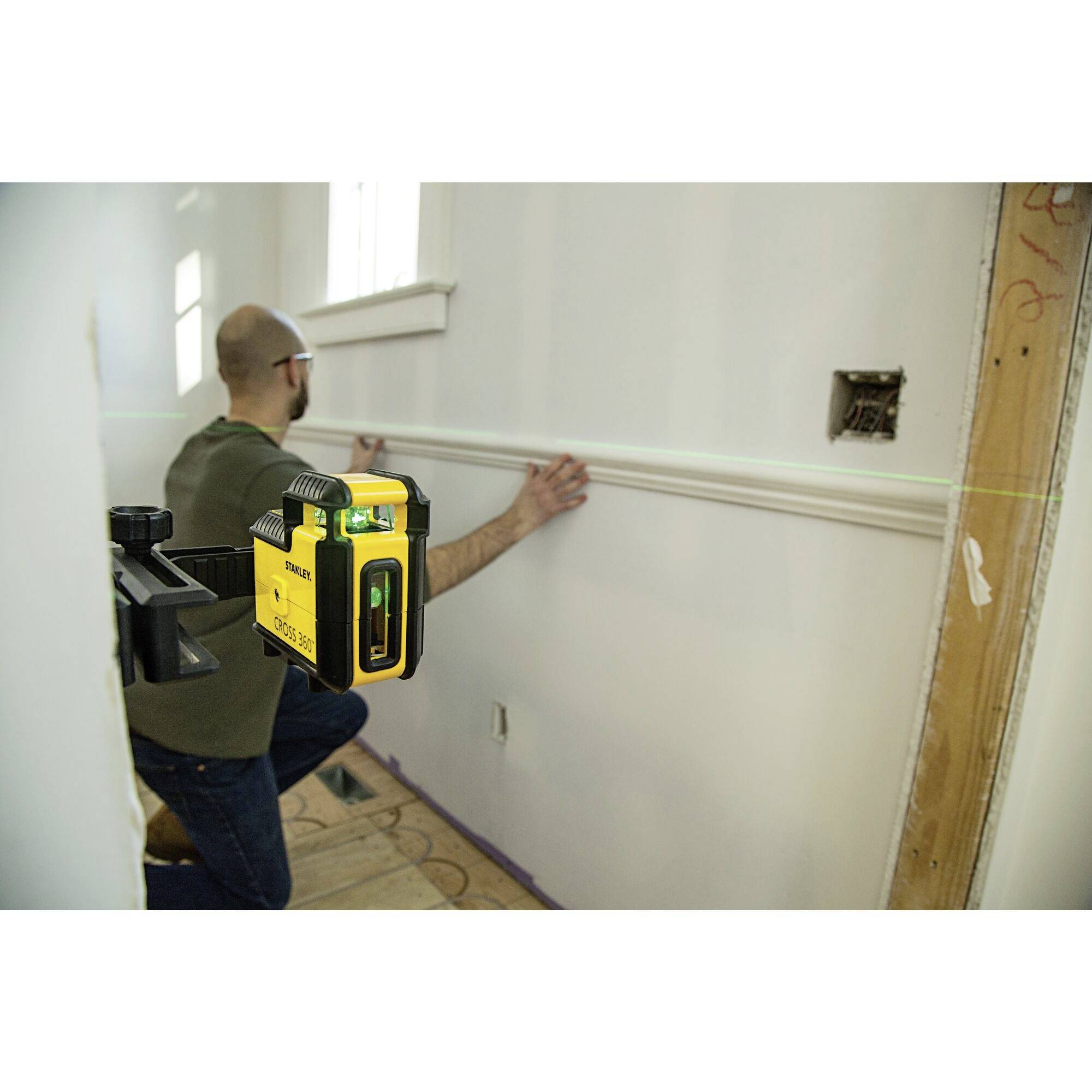 Une personne utilise un niveau laser vert pour installer un revêtement mural dans une pièce.