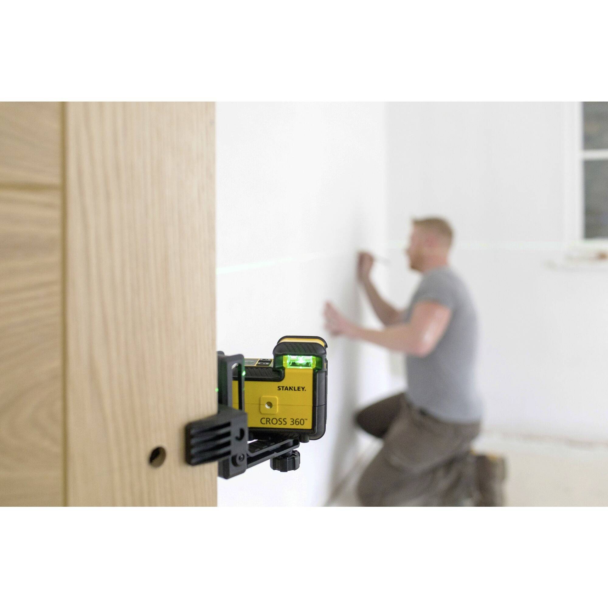 Un homme trace une ligne sur un mur à l'aide d'un outil laser au premier plan, en préparation de travaux muraux.