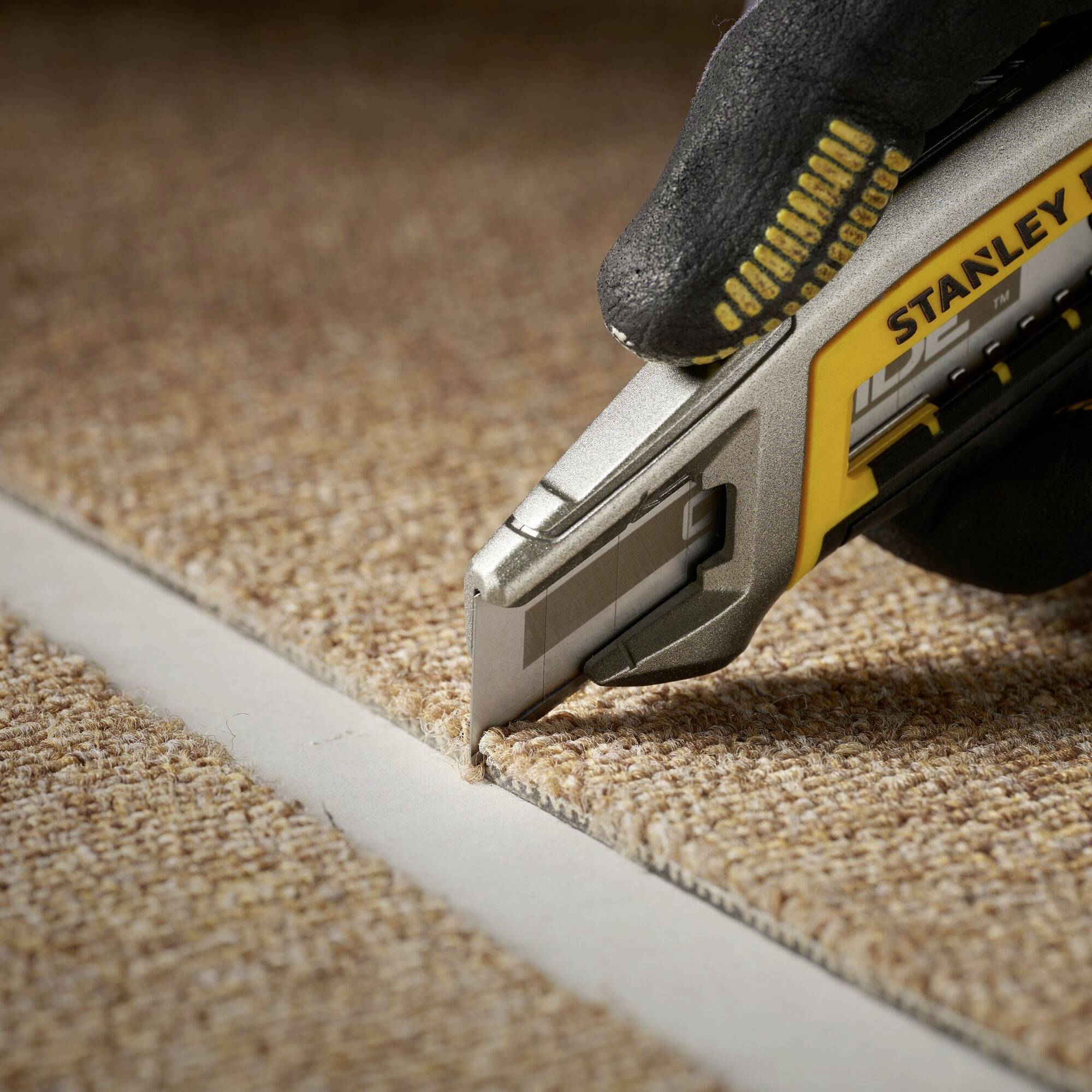 Une personne coupe un tapis avec un couteau à moquette le long d'un bord.